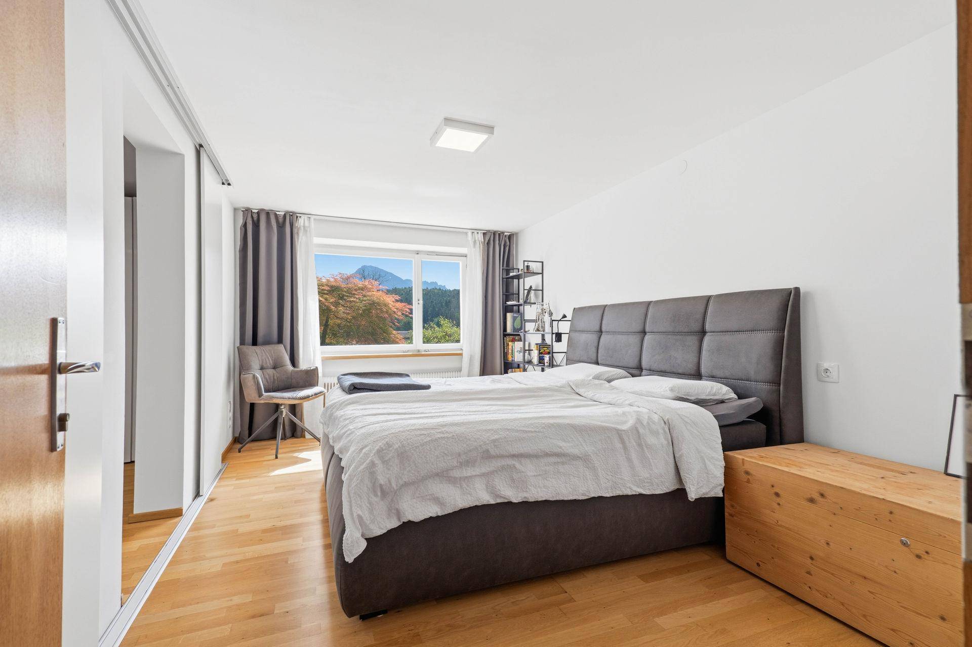 Schlafzimmer mit großem Bett, Holzboden und Fenster mit Bergblick.