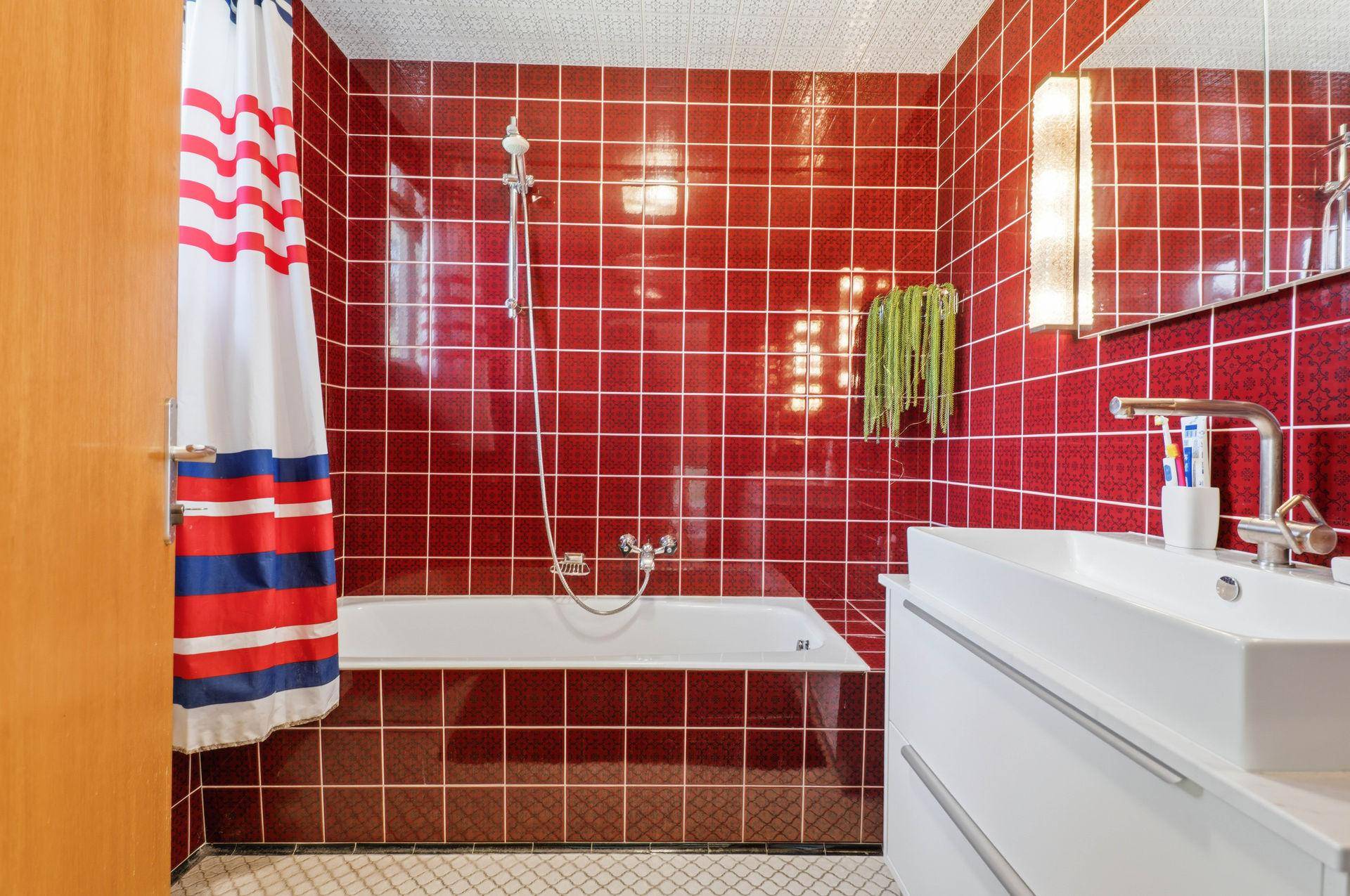 Badezimmer mit roten Fliesen, Badewanne und modernem Waschtisch.
