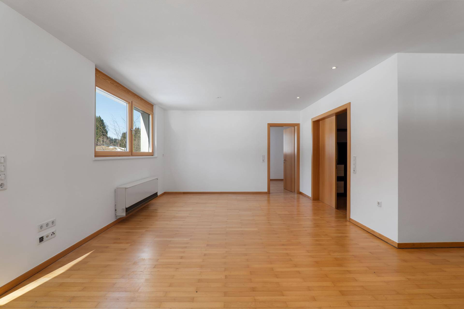 Heller, leerer Raum mit Holzboden und großen Fenstern, bereit zur individuellen Gestaltung.