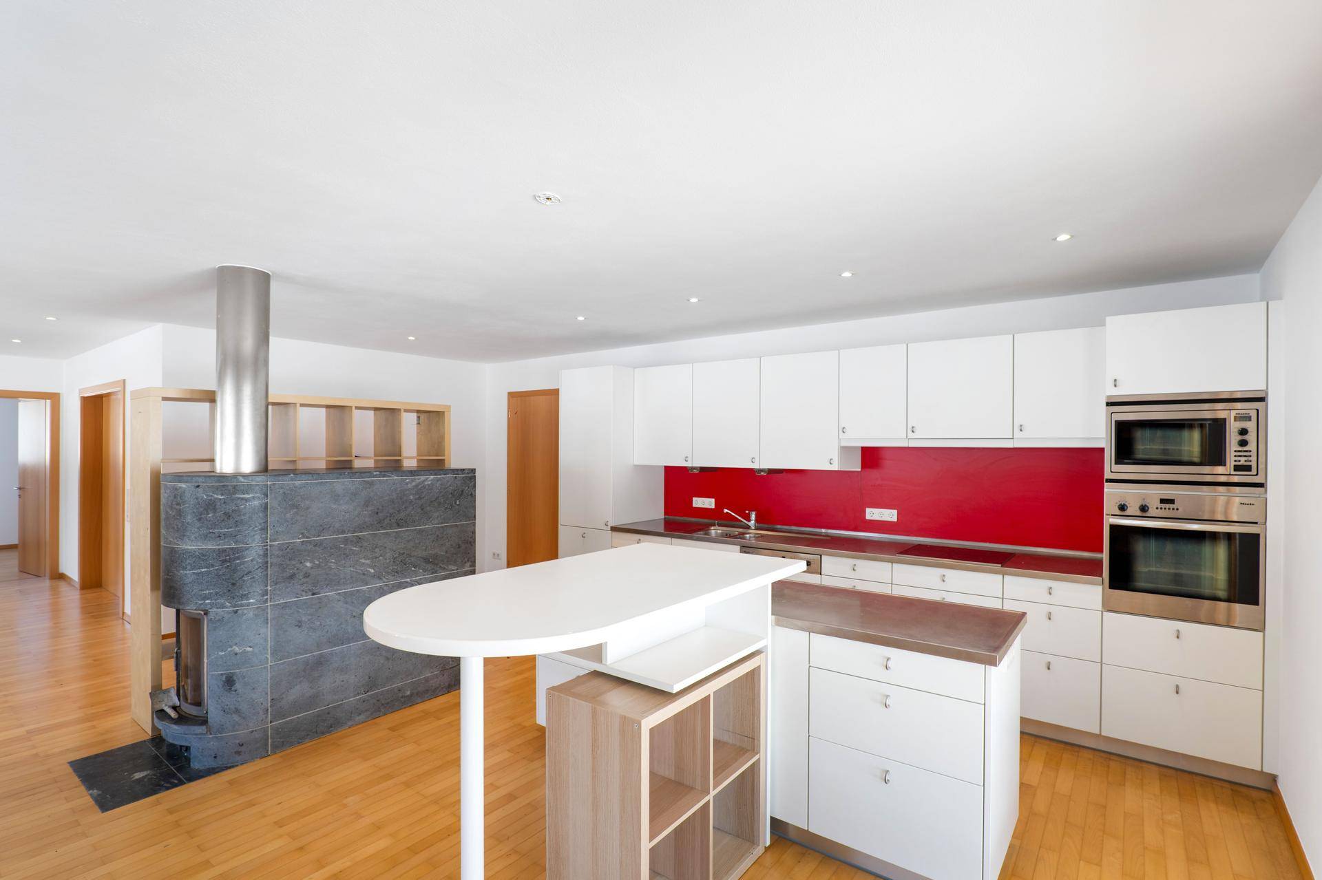 Moderne Küche mit weißen Schränken, roter Rückwand, Kücheninsel und einem Kaminofen.