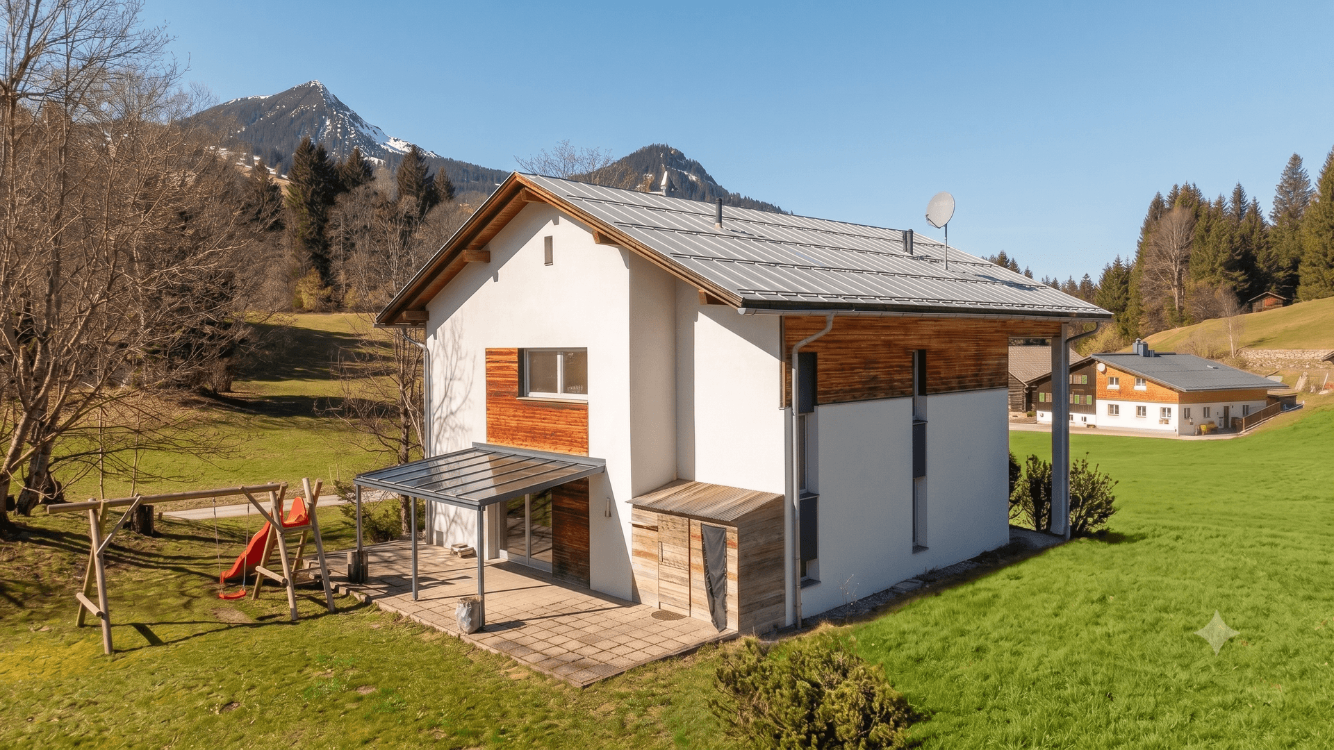 Modernes Haus mit Satteldach, Terrasse und Kinderspielplatz in alpiner Umgebung.