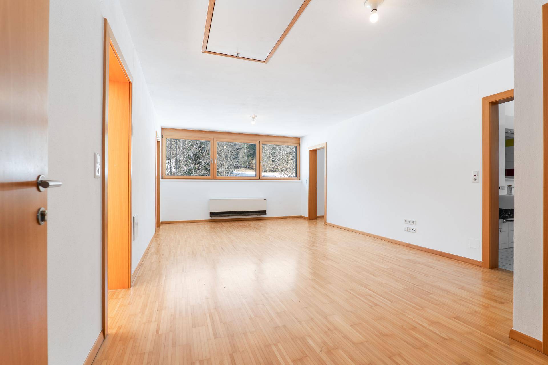 Geräumiger, heller Raum mit Holzboden, Fenstern und Zugang zum Dachboden.