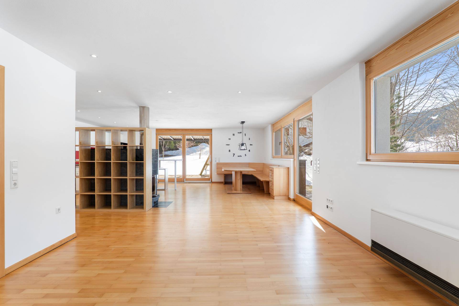 Heller Wohnbereich mit Holzboden, großen Fenstern und einer gemütlichen Holzsitzgruppe.