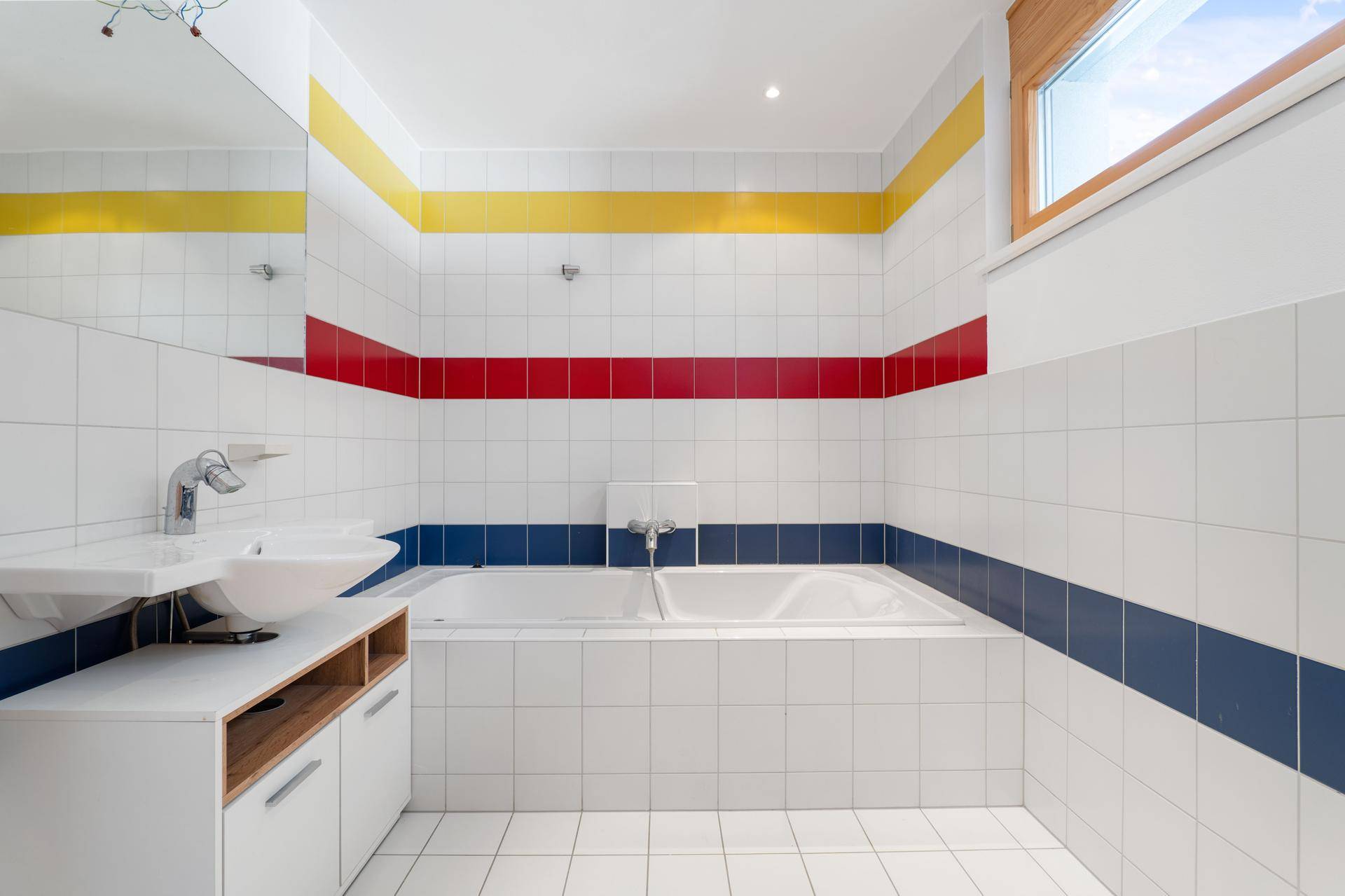 Badezimmer mit Badewanne, Waschbecken und auffälligen farbigen Fliesenstreifen.
