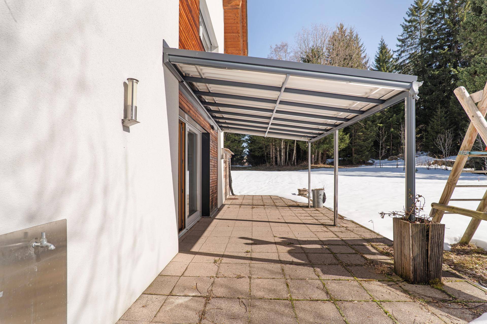 Überdachte Terrasse mit Steinplatten und Blick auf die verschneite Landschaft.
