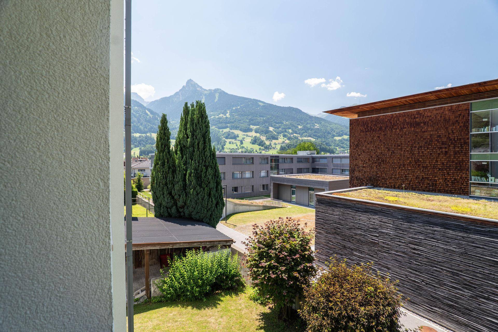 Blick von der Immobilie auf moderne Gebäude, Bäume und die beeindruckende Bergkulisse.