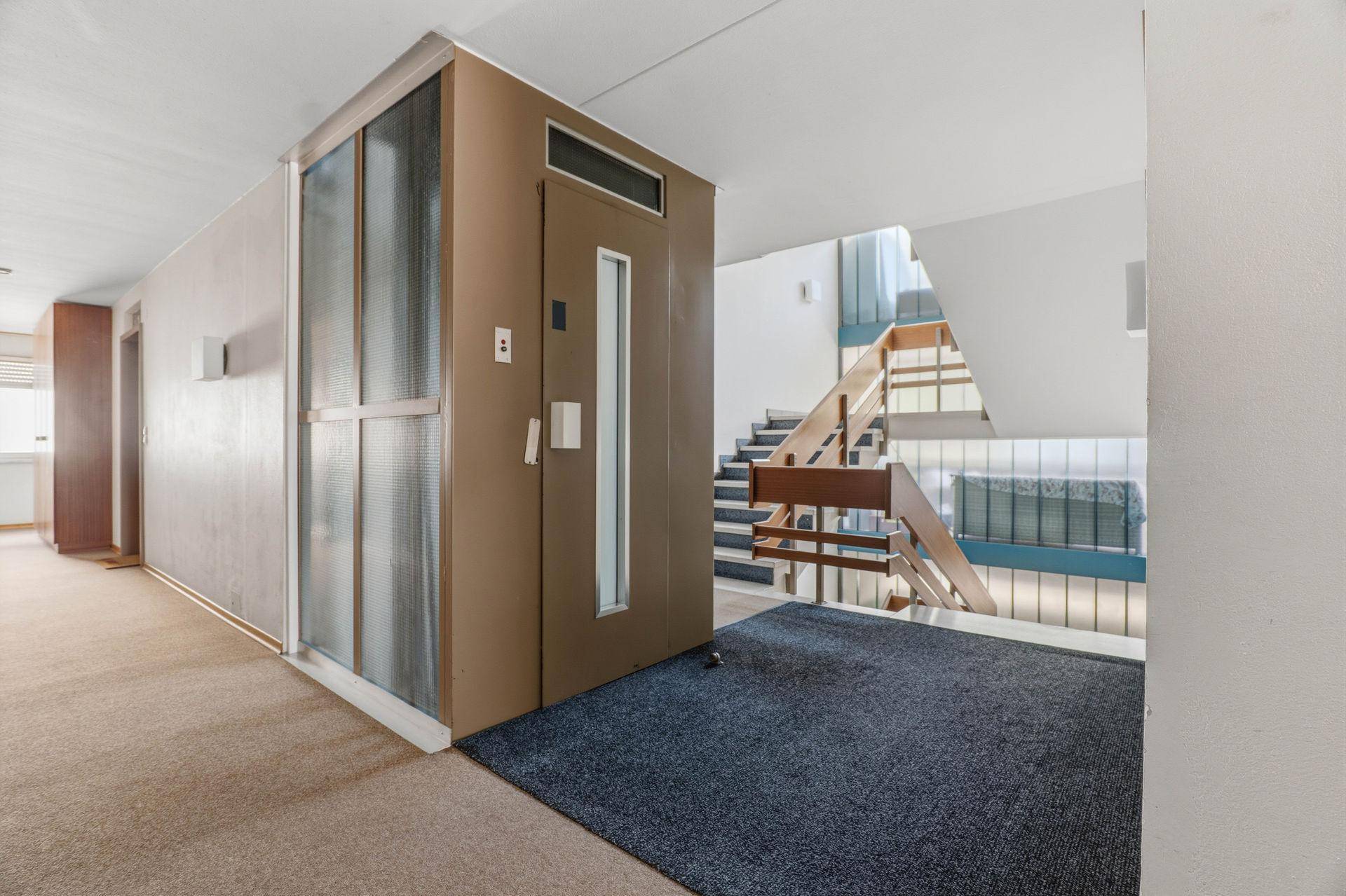 Gemeinschaftsbereich mit Aufzug und Treppenhaus, ausgestattet mit Teppichboden und Holzgeländer.