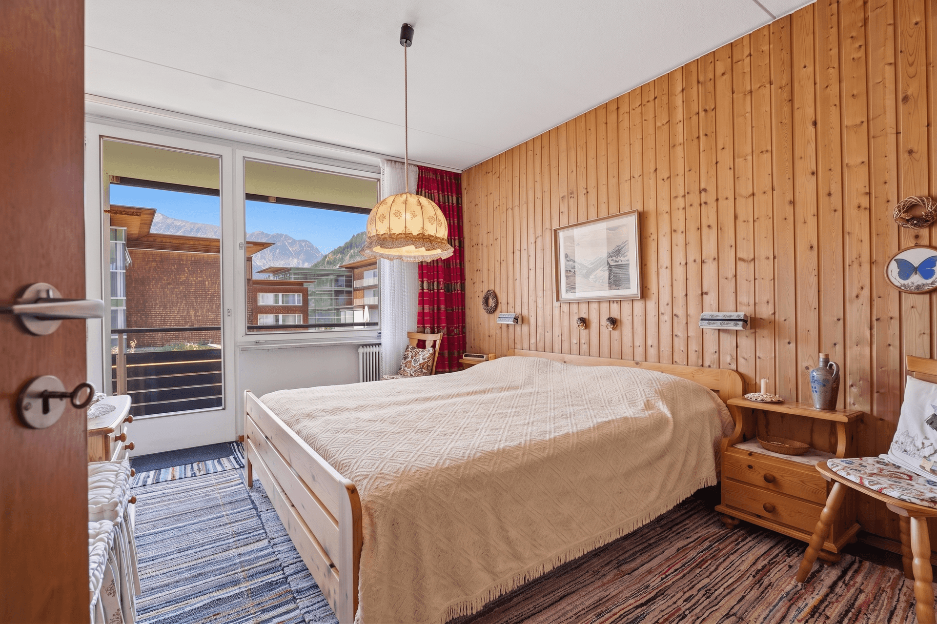 Gemütliches Schlafzimmer mit Holzvertäfelung, Doppelbett und Zugang zum Balkon mit Bergblick.