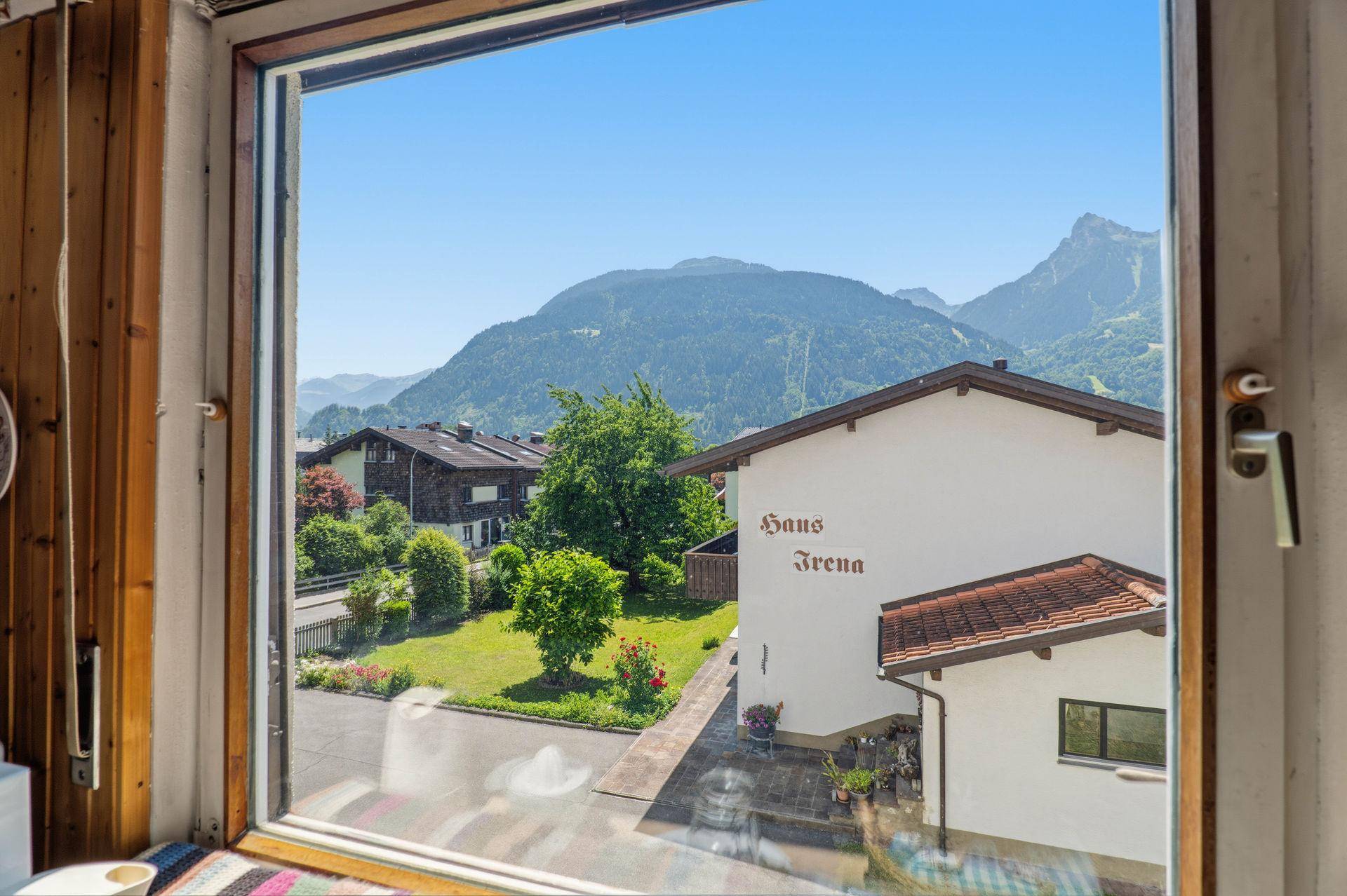 Blick aus dem Fenster auf einen gepflegten Garten und die umliegende Berglandschaft.