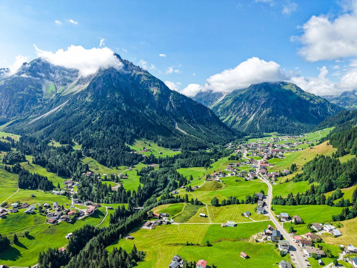 Weitläufige Luftaufnahme eines grünen Tals mit Siedlungen und majestätischen Bergen.