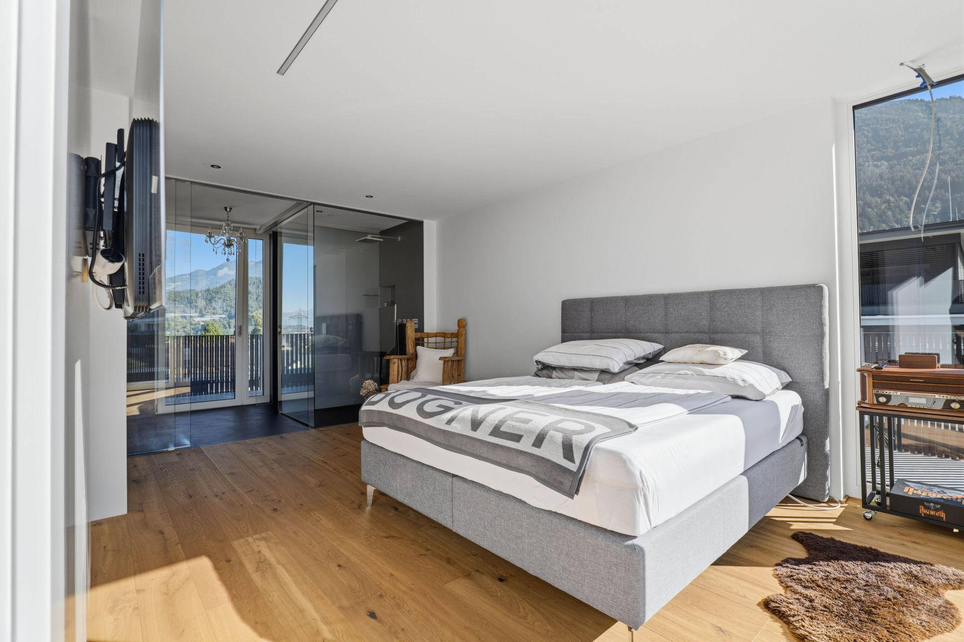 Helles Schlafzimmer mit Doppelbett, Holzboden und Glaswand zum Badezimmer.
