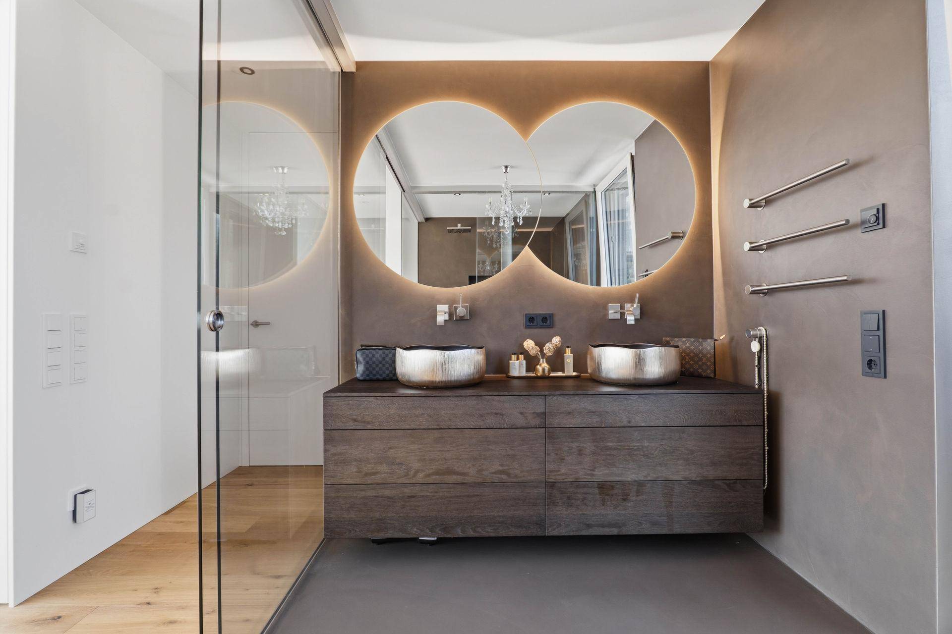 Elegantes Badezimmer mit zwei runden, beleuchteten Spiegeln und stilvollen Aufsatzwaschbecken.