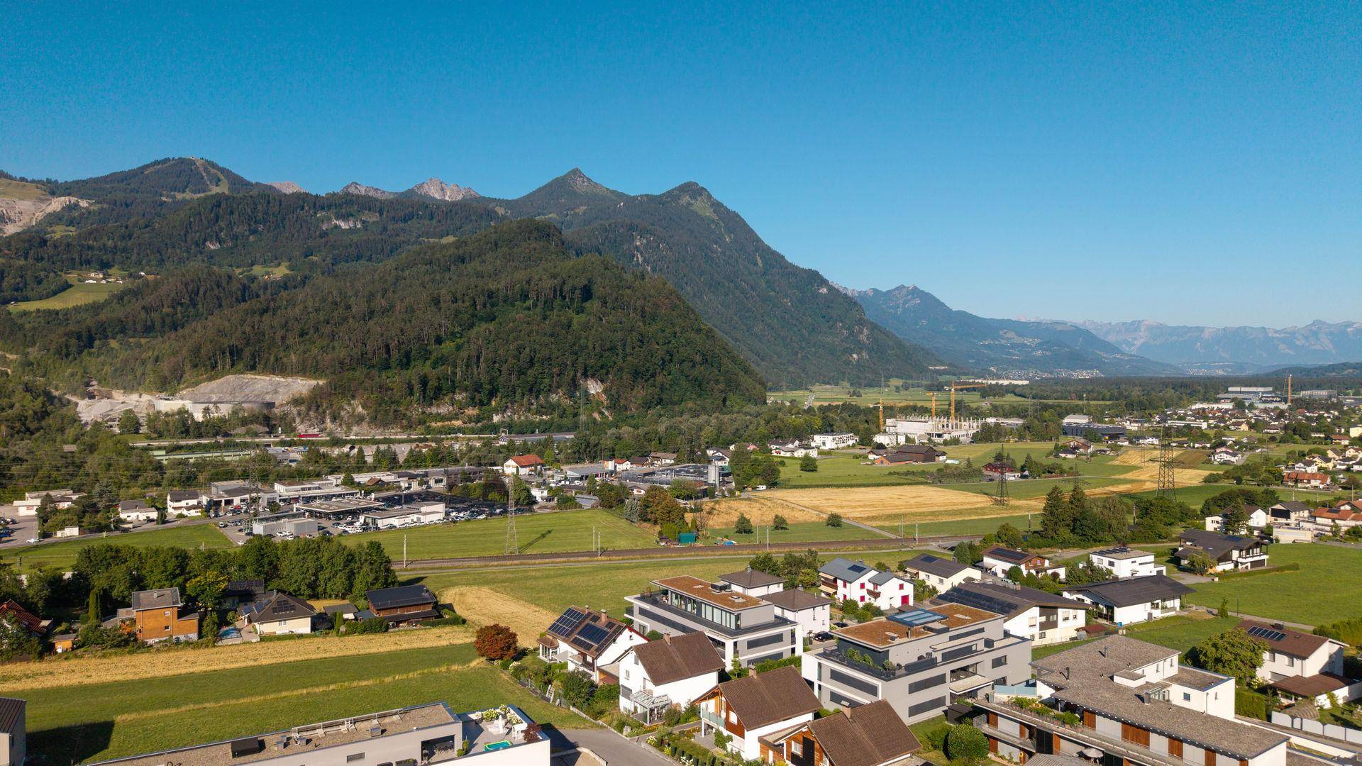 Ausgedehnte Luftaufnahme des Tals mit Feldern, Wohngebieten und einer weiten Bergkette.
