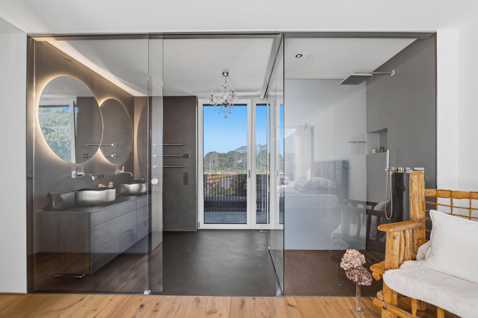 Modernes Badezimmer, durch Glaswand vom Schlafzimmer getrennt, mit Doppelwaschbecken und Bergblick.