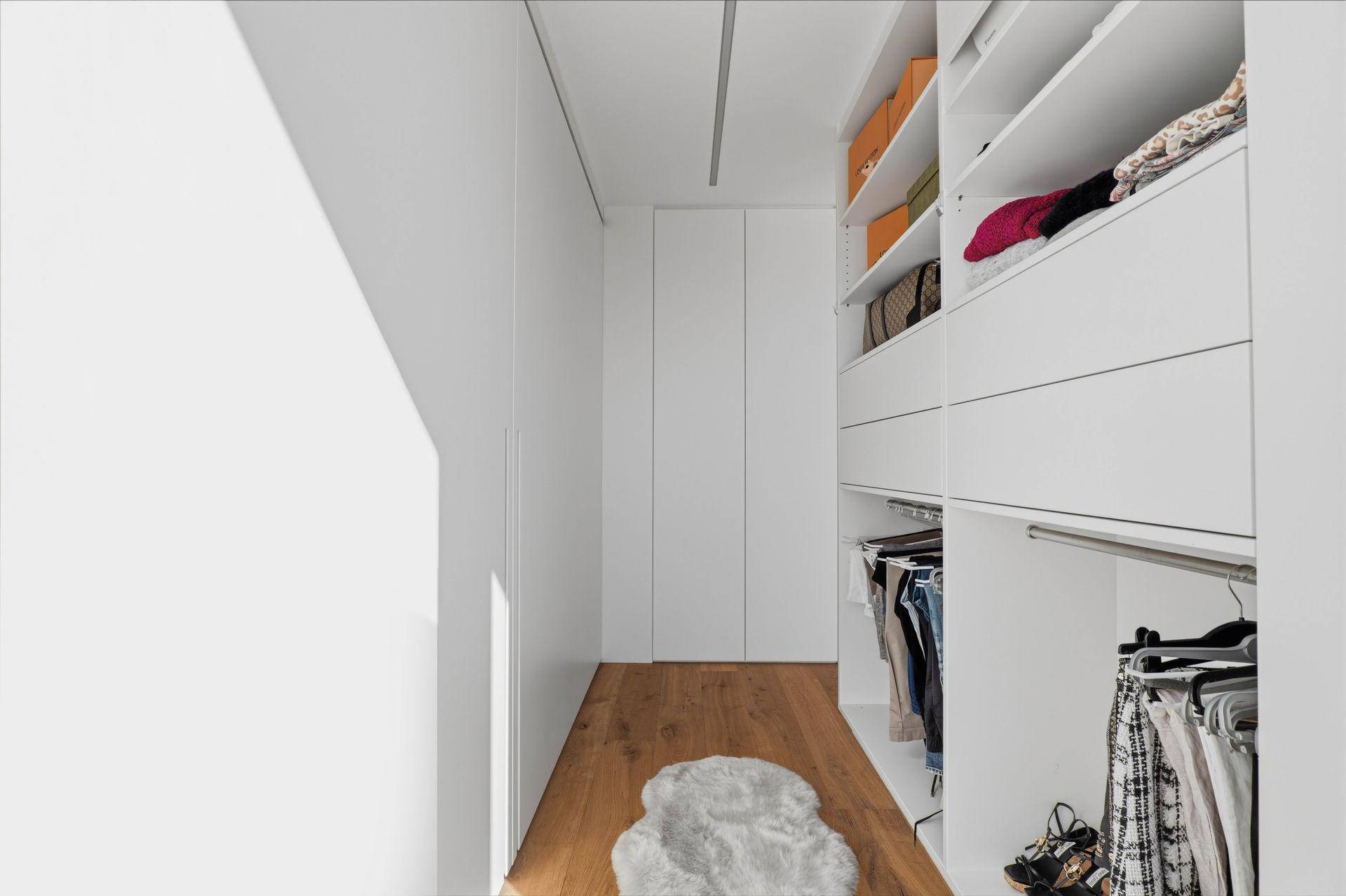 Geräumiger begehbarer Kleiderschrank mit integrierten Schränken und Holzfußboden.