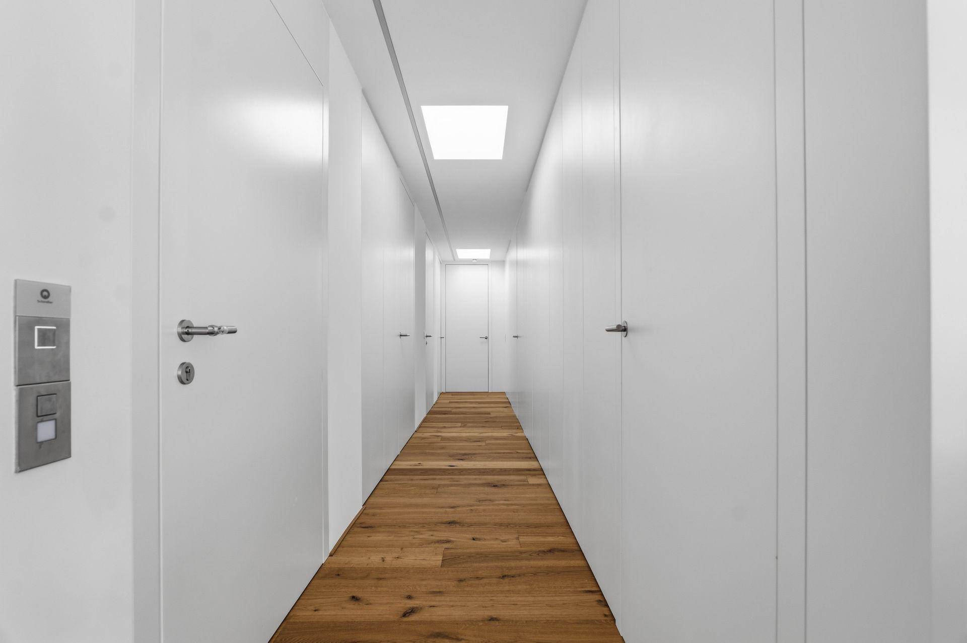 Langer, heller Flur mit Holzfußboden und vielen weißen Türen.