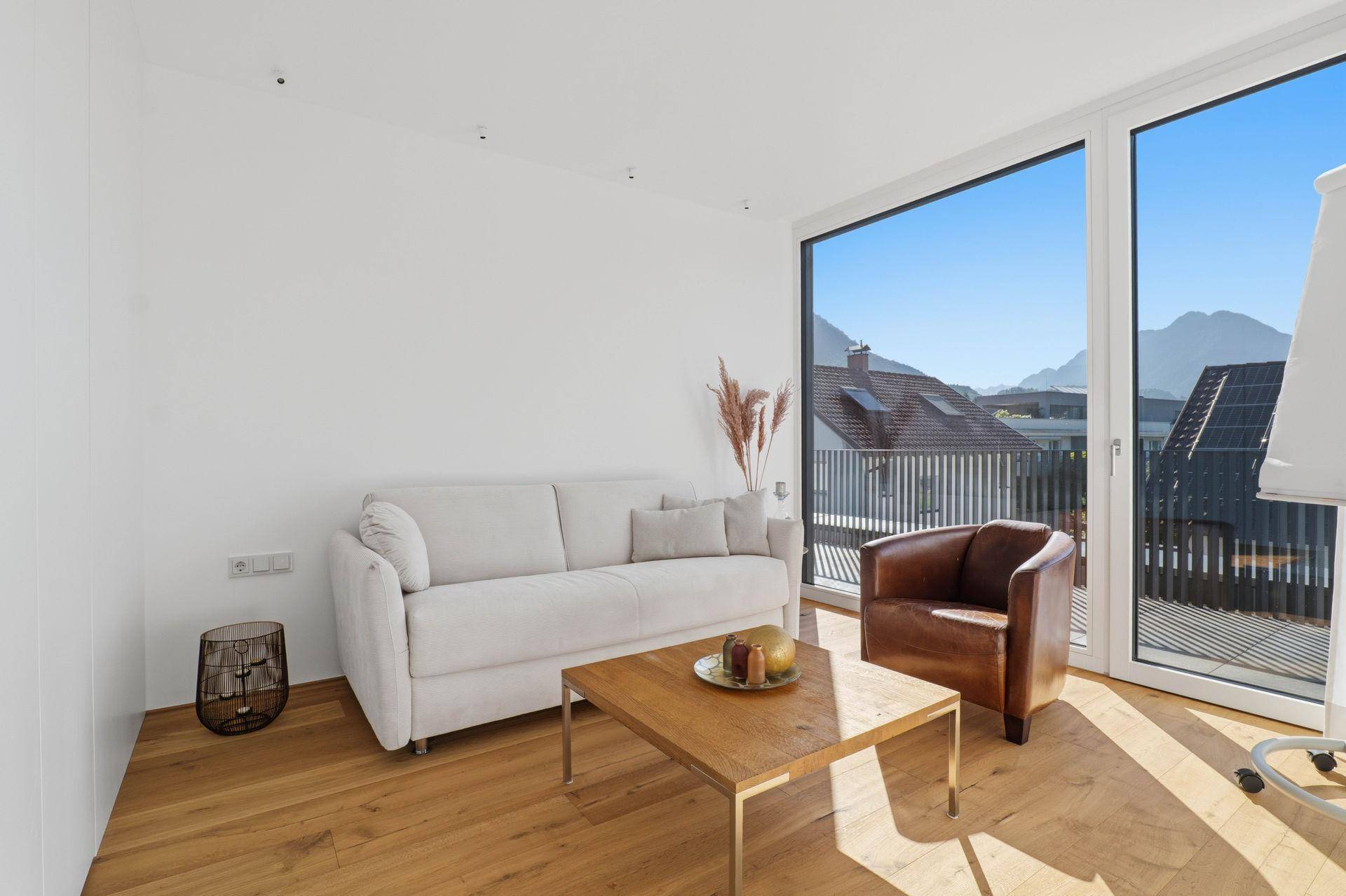 Gemütliches Wohnzimmer mit Sofa, Ledersessel und Holztisch, hell und modern eingerichtet.