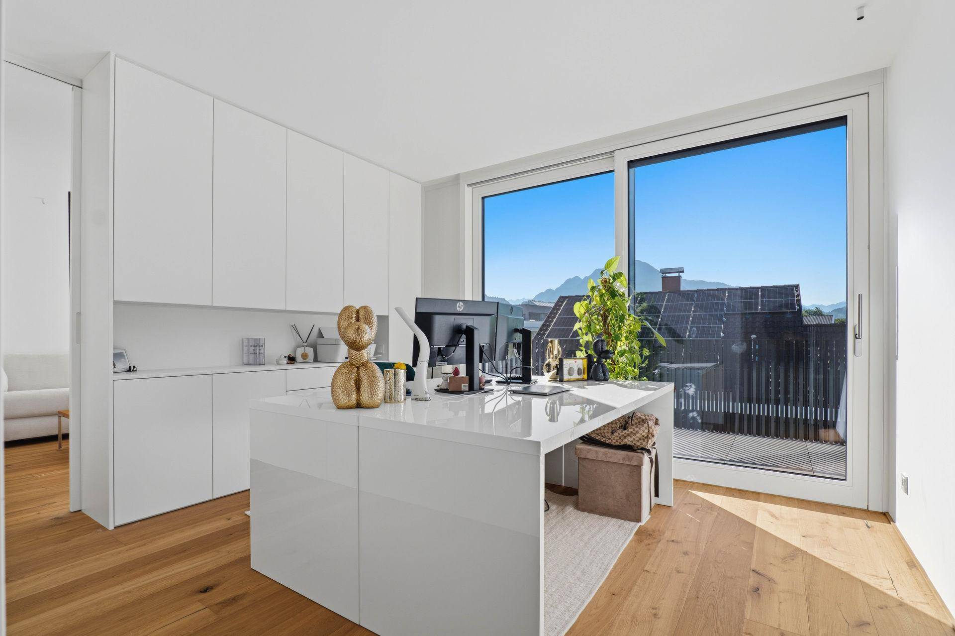 Helles Büro mit großem Schreibtisch, weißen Schränken und Bergblick von der Terrasse.