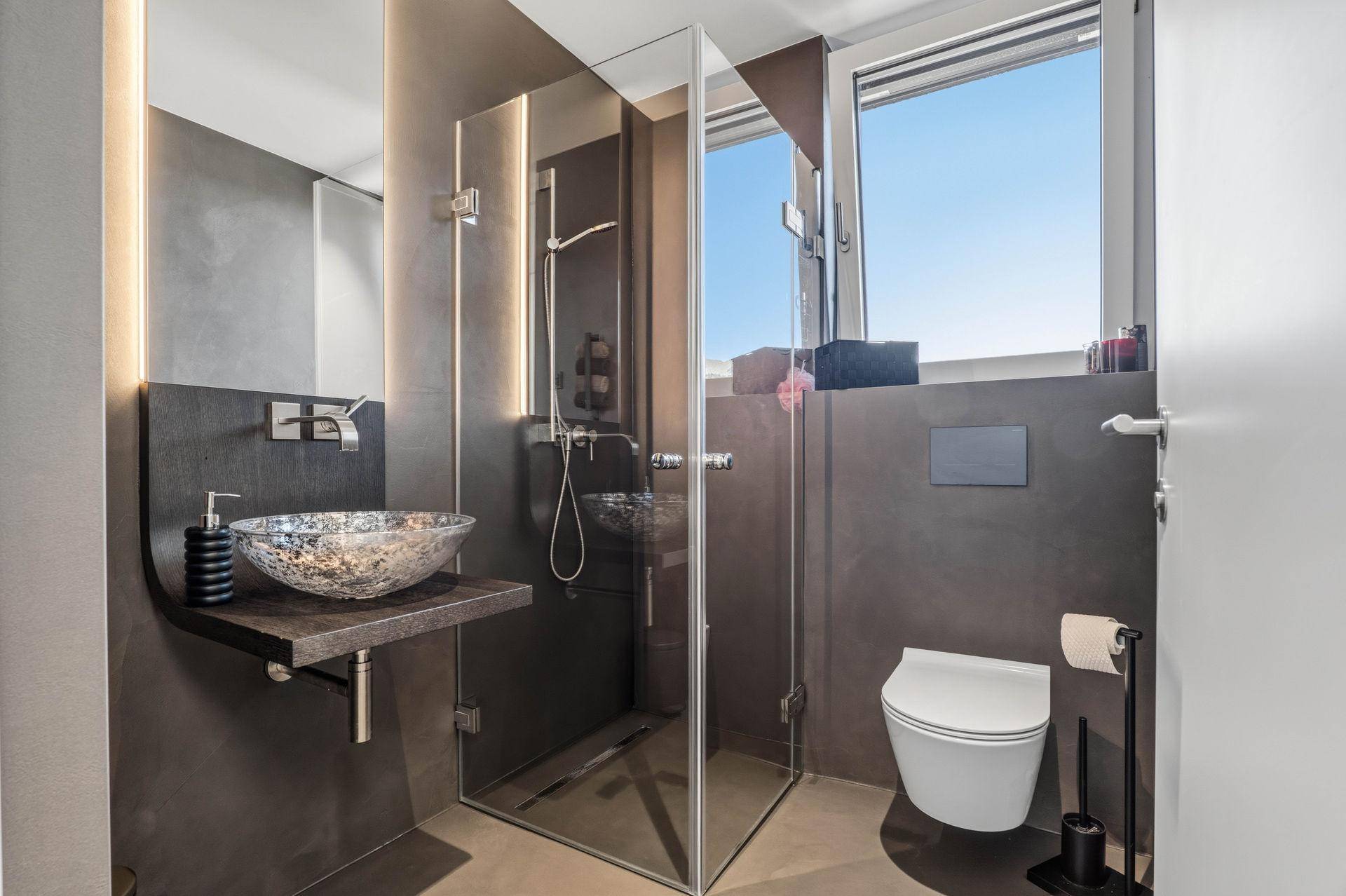 Modernes Badezimmer mit Duschkabine, Aufsatzwaschbecken und wandhängendem WC.