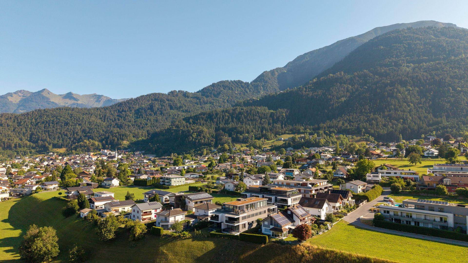 Weitwinkelaufnahme der Siedlung mit vielen Häusern und üppiger Berglandschaft im Hintergrund.