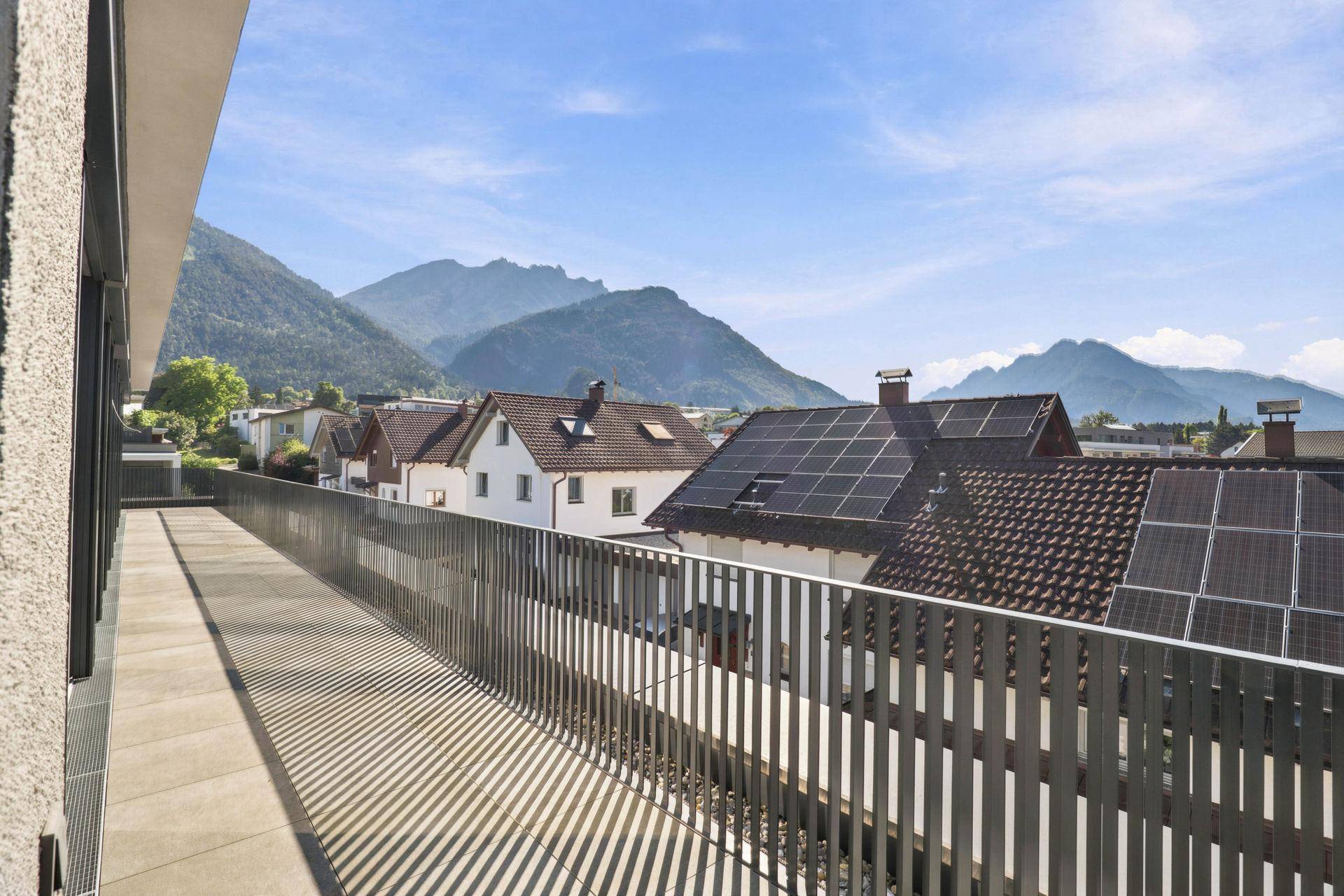 Geräumige Terrasse mit Blick auf benachbarte Dächer mit Solaranlagen und die Berglandschaft.