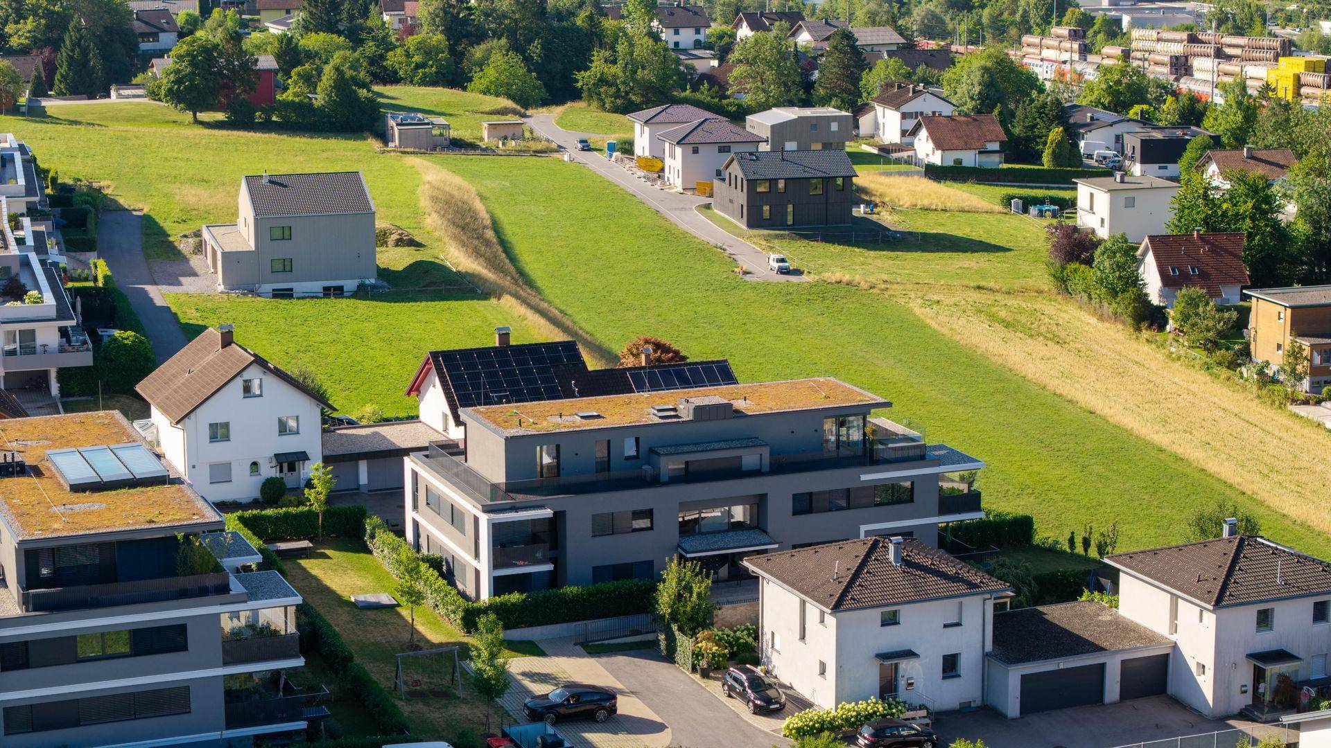 Weitläufige Luftaufnahme der Wohngegend mit Neubauten, Wiesen und angrenzenden Bergen.