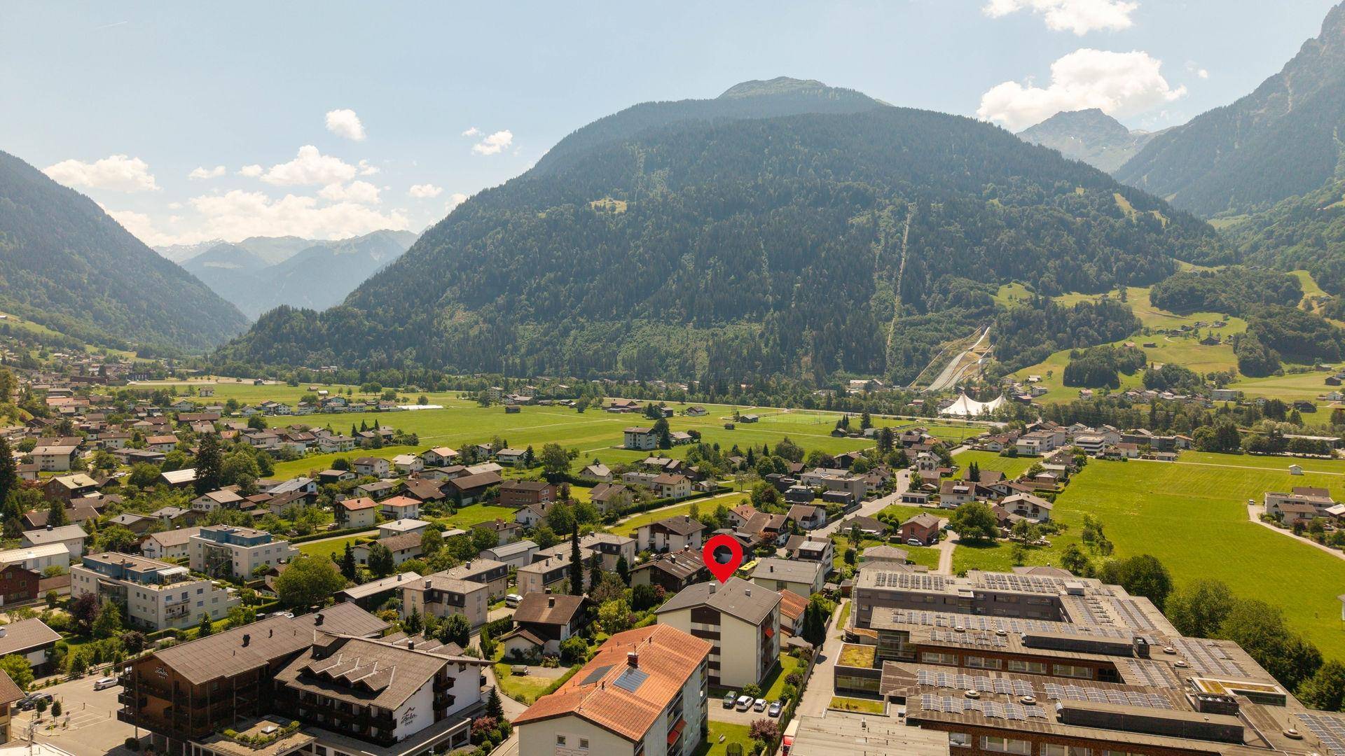 Panoramische Luftaufnahme der Siedlung mit Bergblick und weitläufigen Grünflächen.