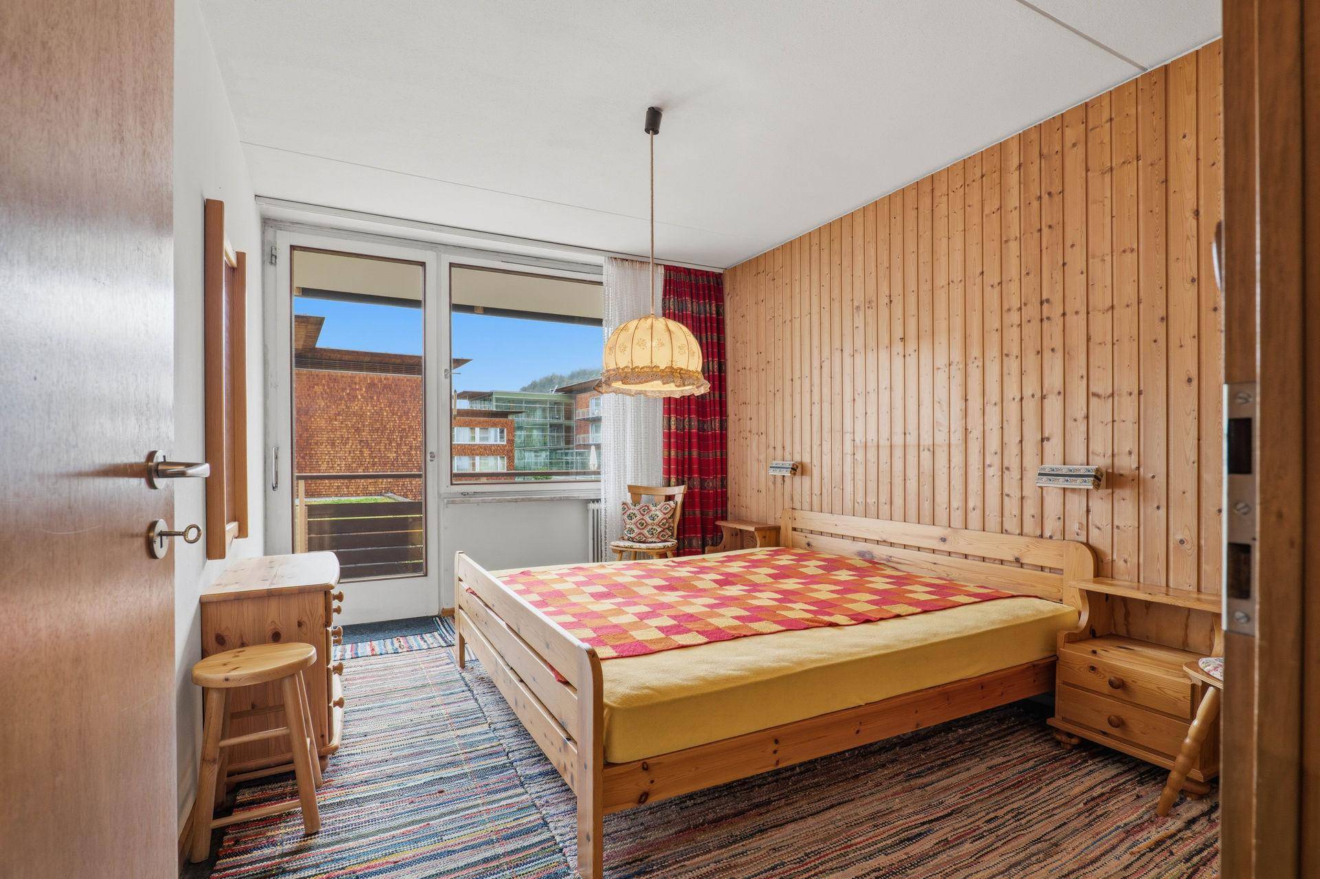 Schlafzimmer im alpinen Stil mit Holzbett, Holztäfelung und Balkonzugang.