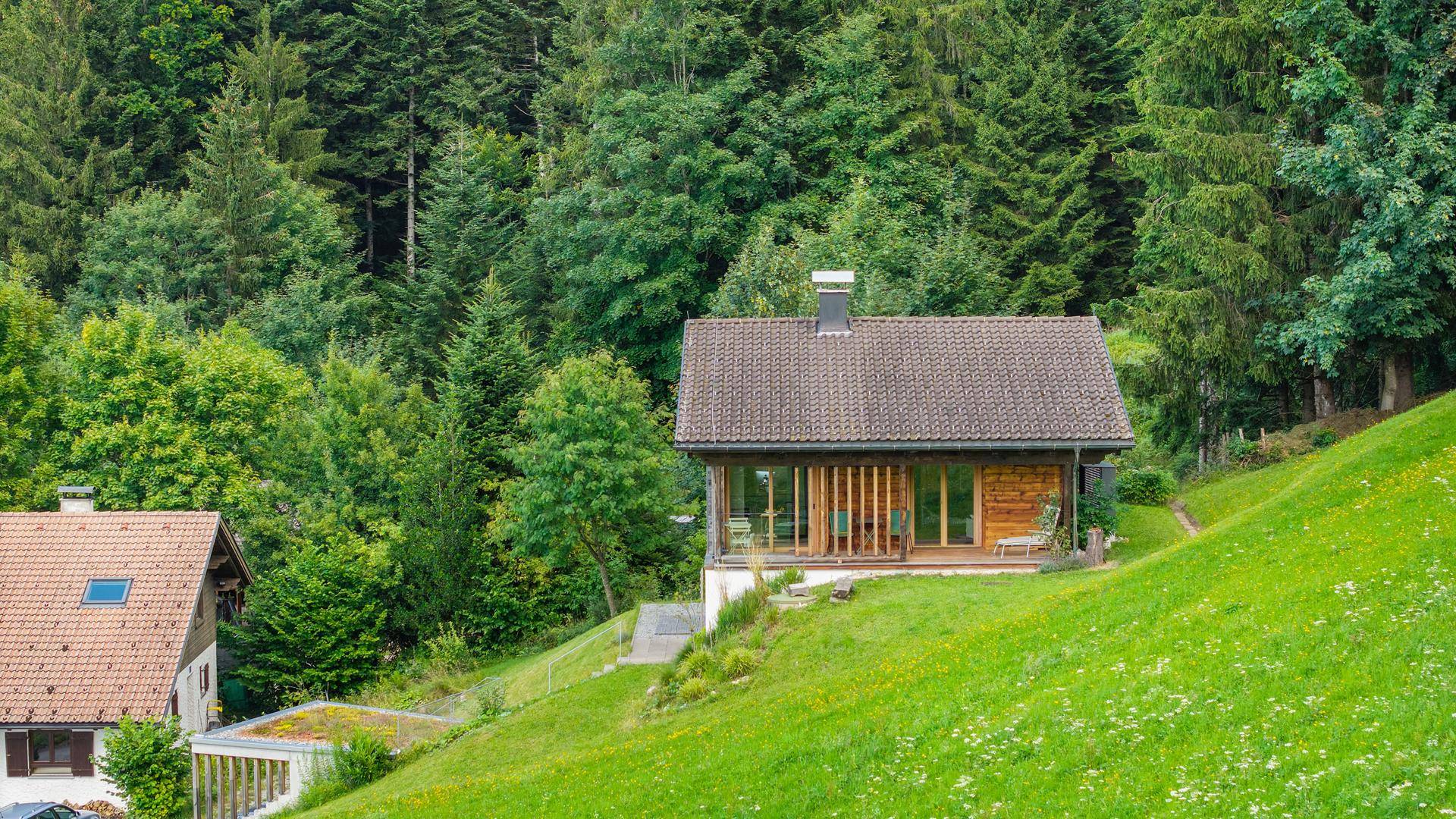 Charmantes Holzhaus in idyllischer Hanglage, umgeben von üppigem Grün und Wald.