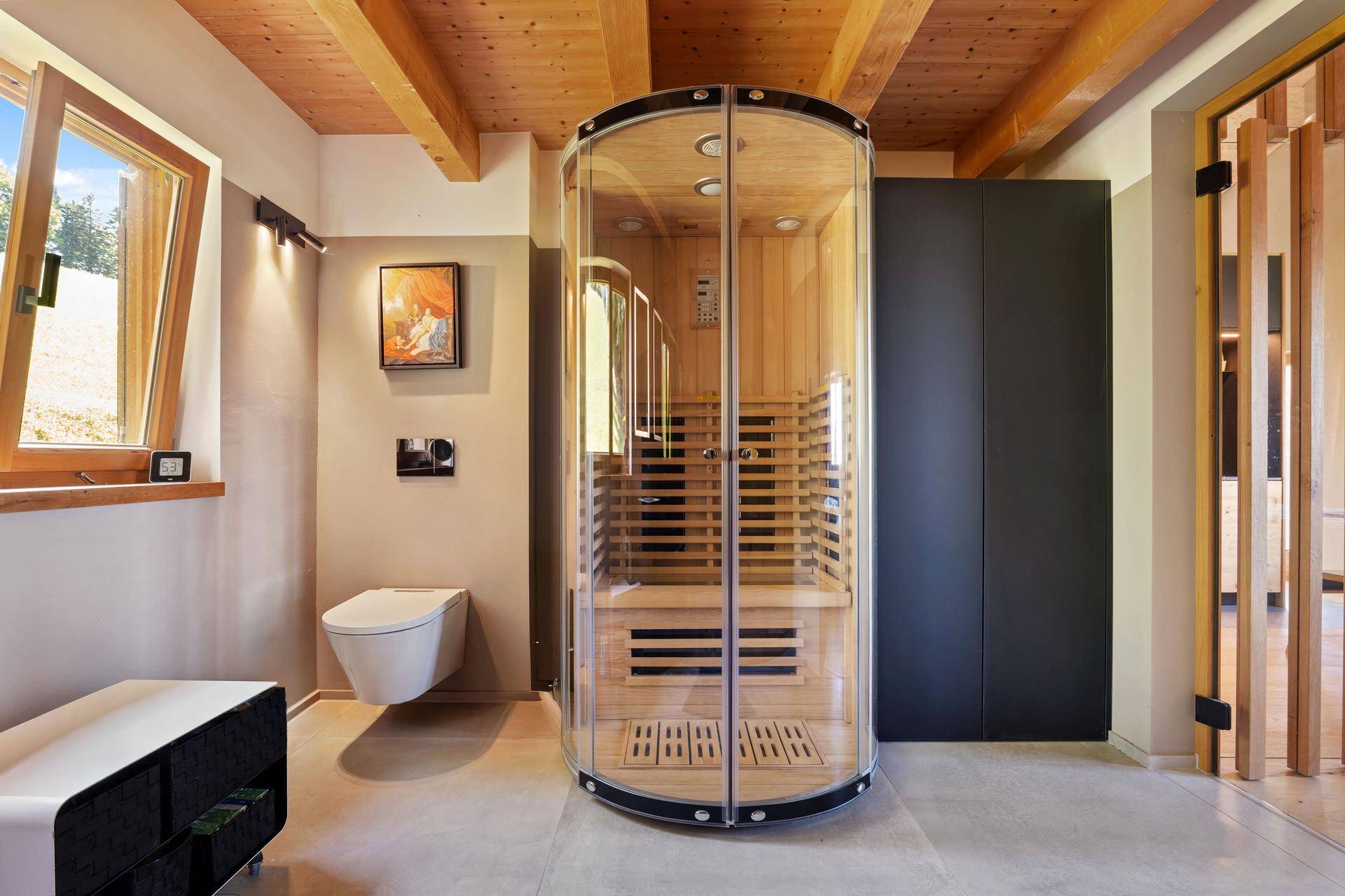 Helles Badezimmer mit moderner Dusch-Sauna-Kombination, Wand-WC und Holzbalkendecke.