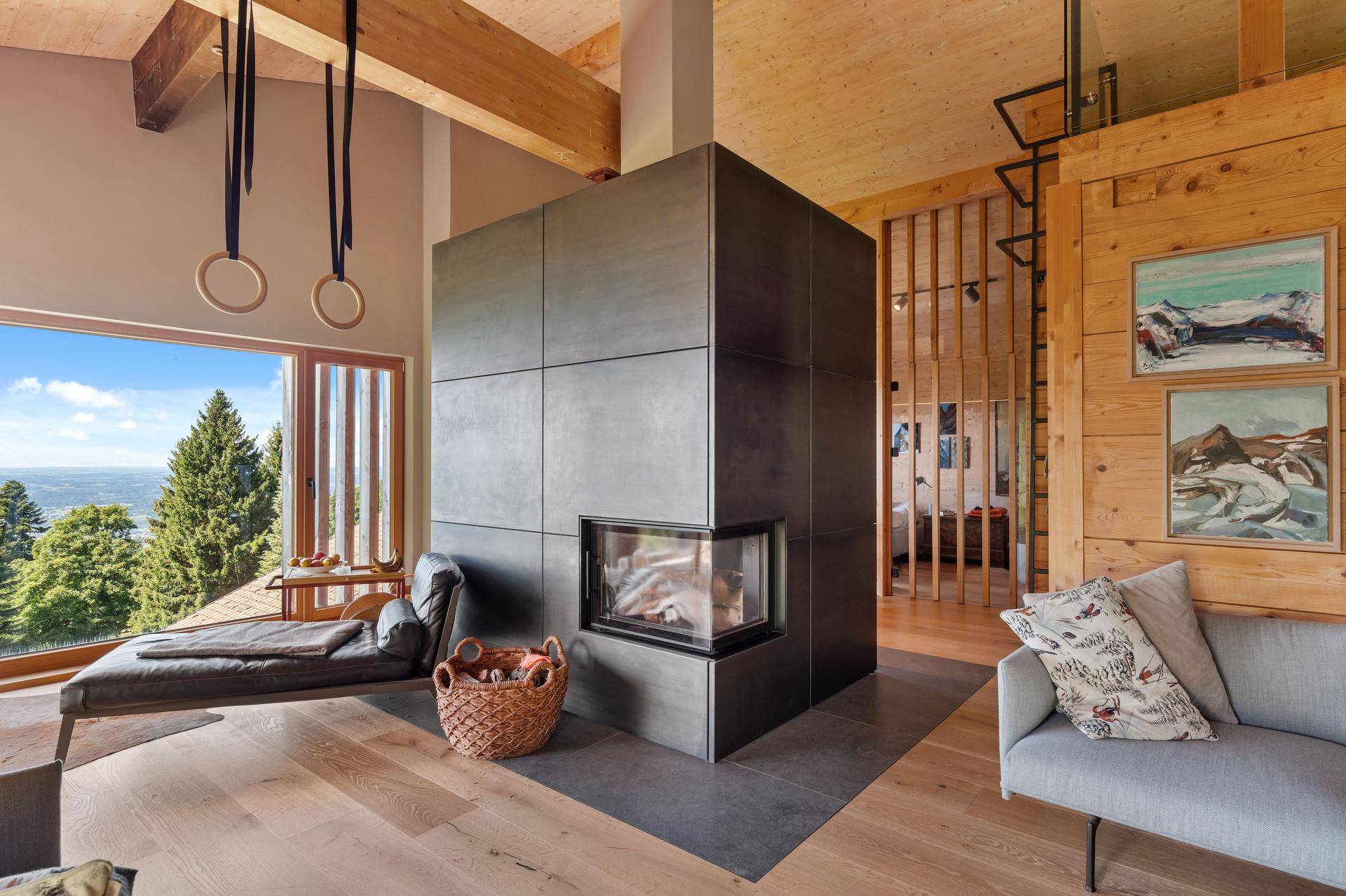 Helles Wohnzimmer mit modernem Kamin, Holzbalken und großen Fenstern mit Panoramablick.