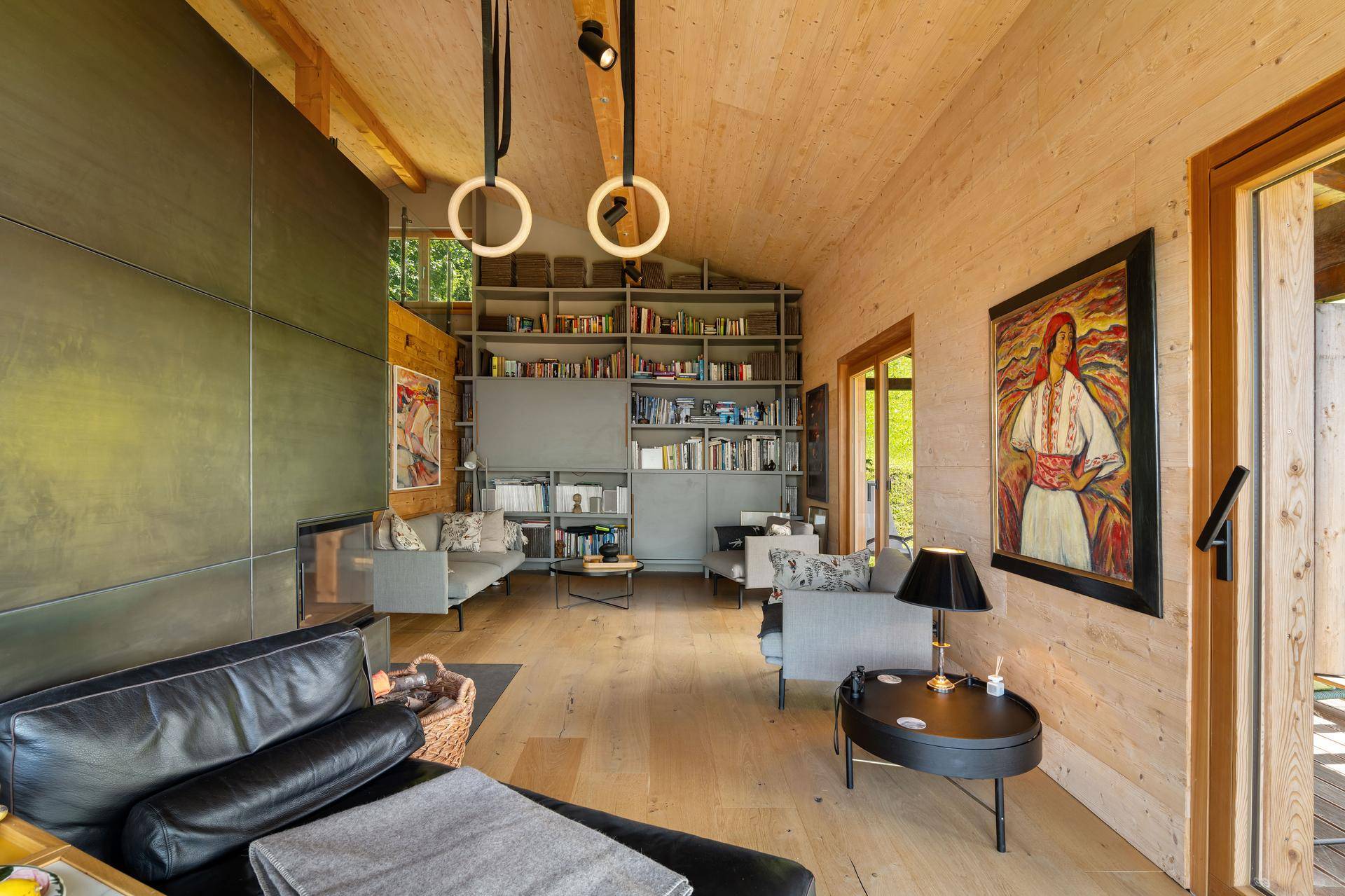 Geräumiges Wohnzimmer mit Holzwänden, Parkettboden, Bücherregalen und modernen Möbeln.