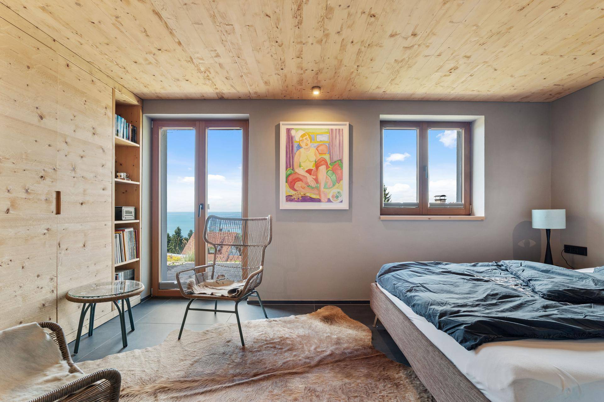 Schlafzimmer mit Holzwänden, großen Fenstern mit Seeblick und einem gemütlichen Bett.