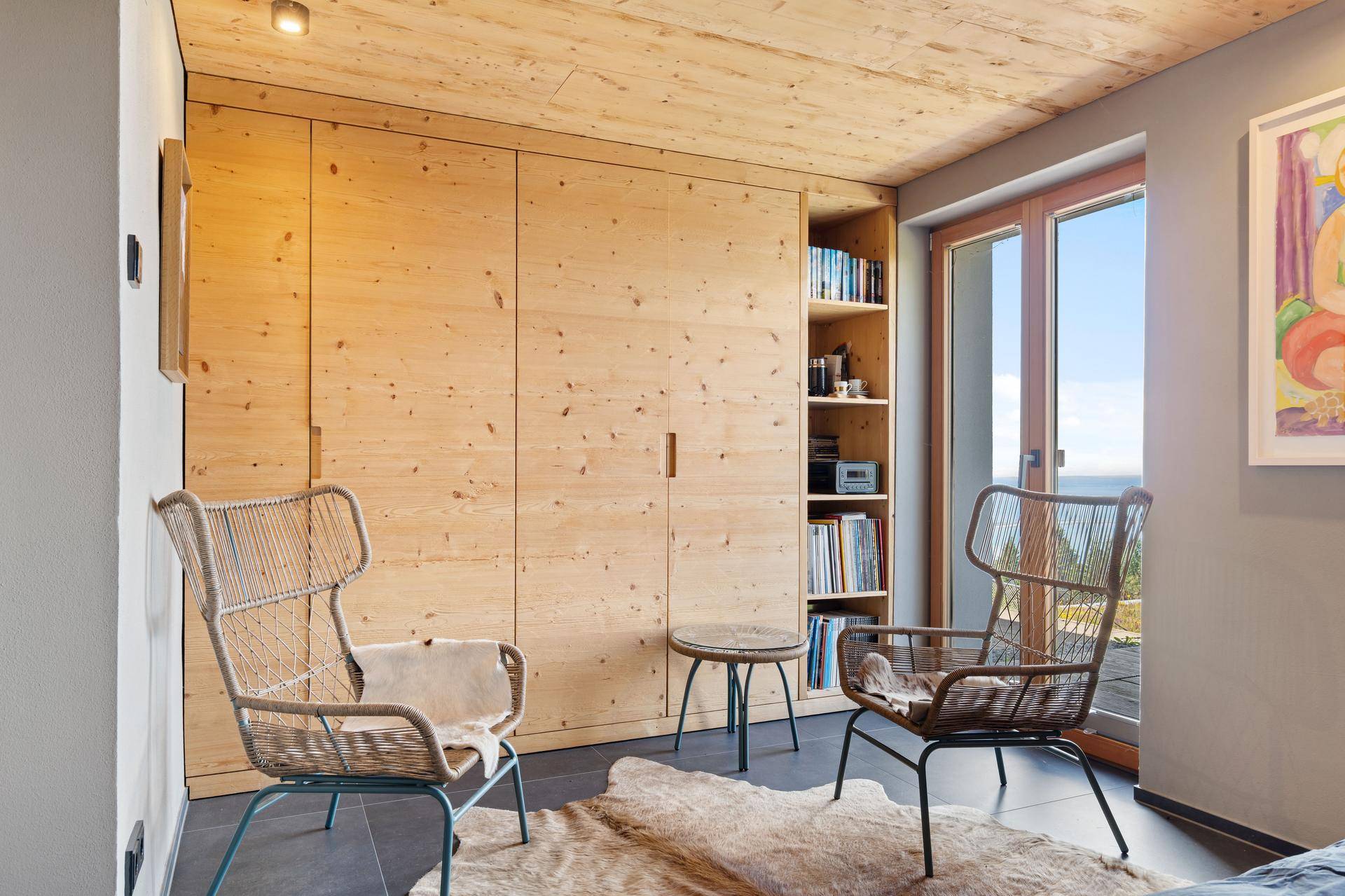 Schlafzimmer mit Einbauschränken aus Holz, gemütlichen Sesseln und Zugang zu einem Balkon.