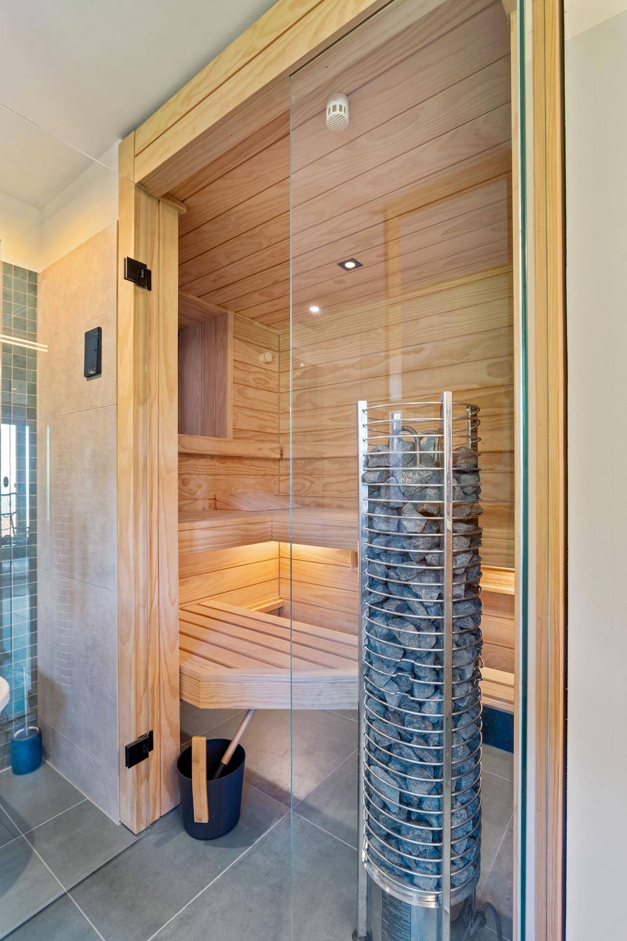 Detailansicht einer modernen Sauna mit Holzbänken und einem großen Saunaofen in einem Badezimmer.