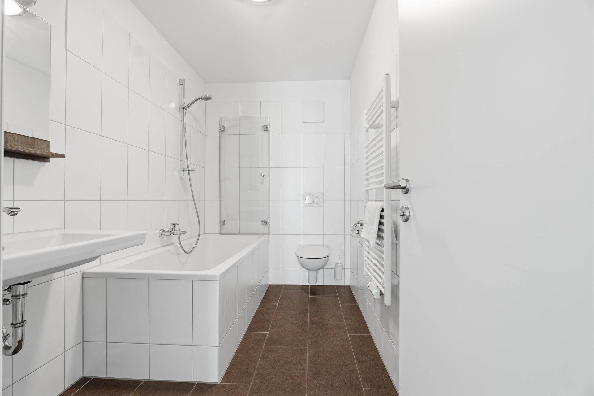 Modernes Badezimmer mit Badewanne, Dusche, WC und Handtuchheizkörper.