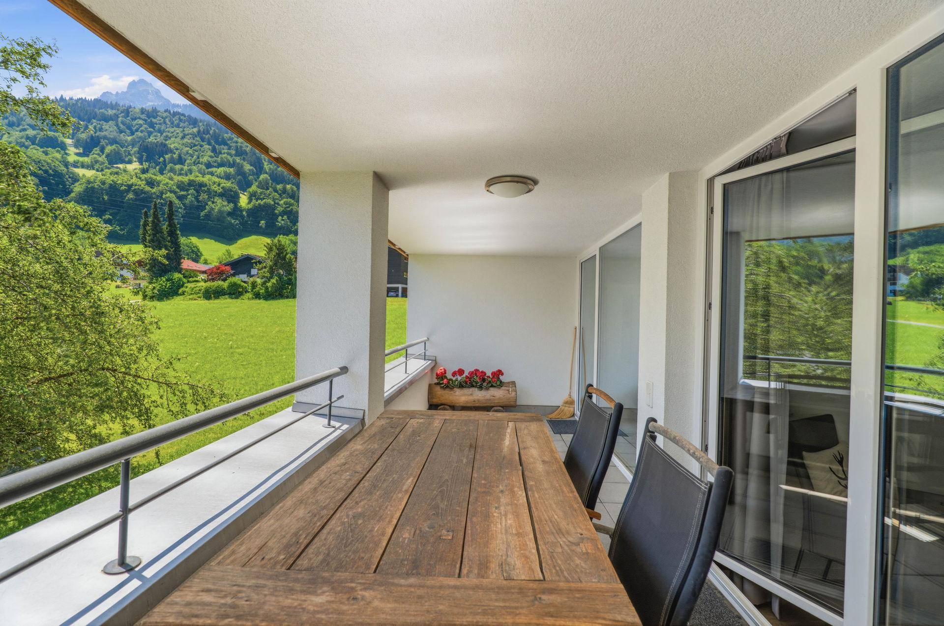 Sonniger Balkon mit Holztisch und Blick auf grüne Wiesen und Berge.