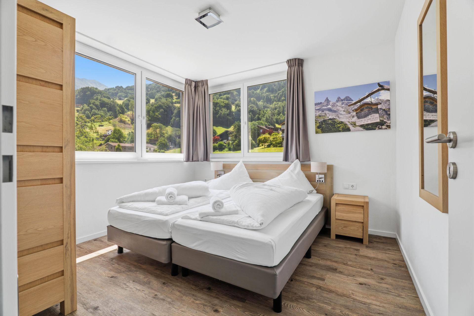 Schlafzimmer mit Bergblick durch große Fenster und Holzboden.