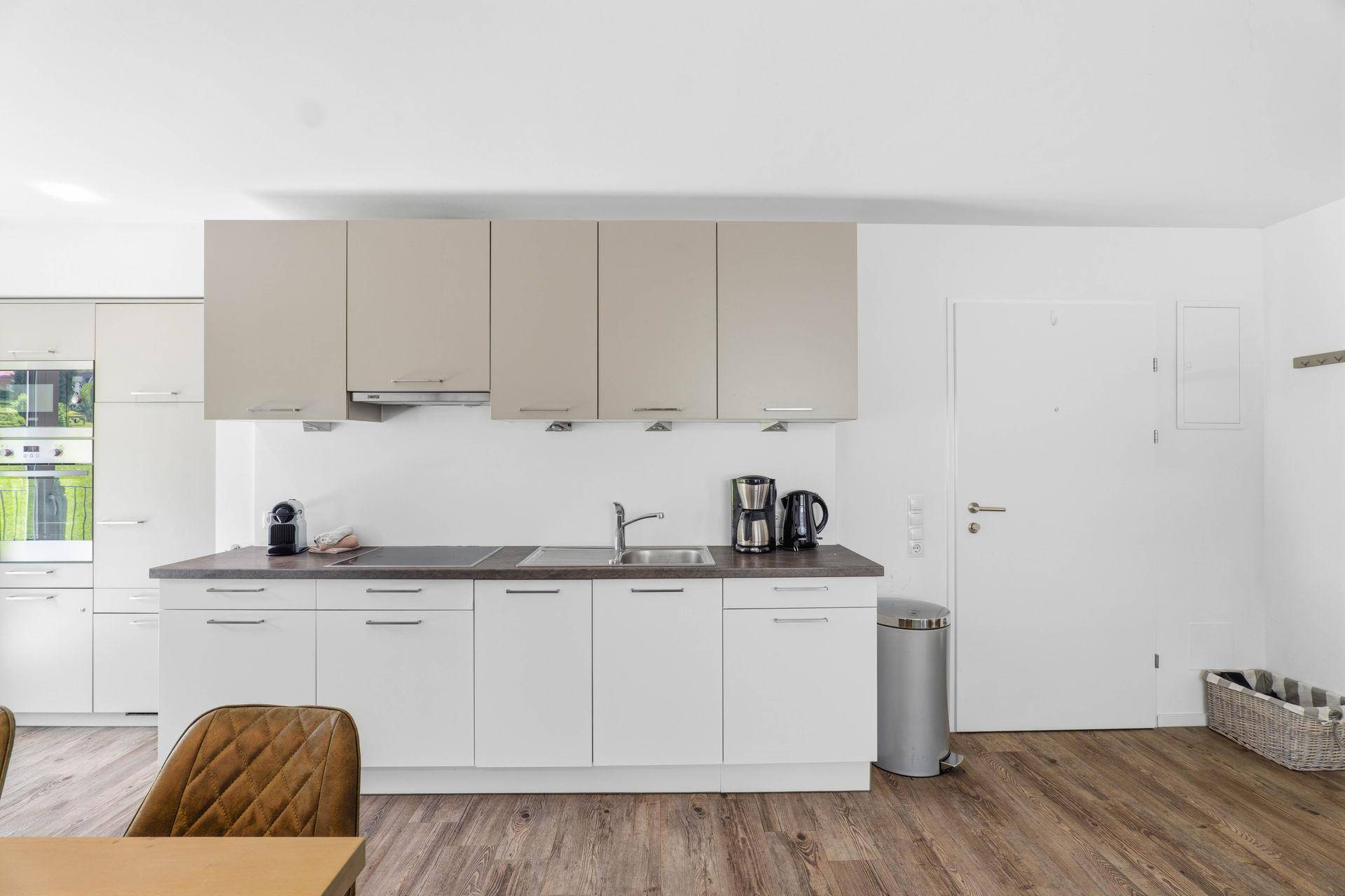 Moderne Einbauküche mit hellen Schränken, Kochfeld und Spüle.