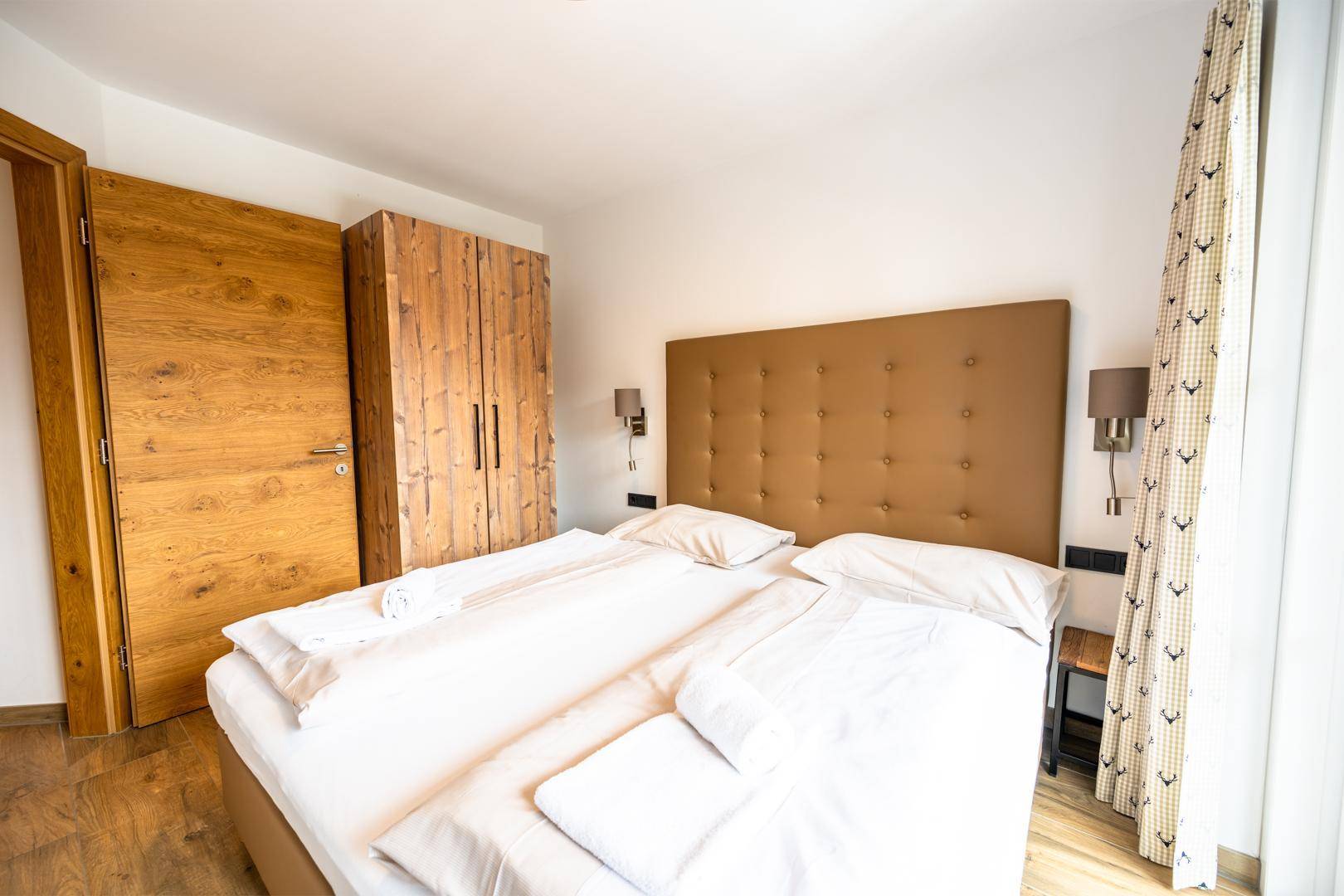 Helles Schlafzimmer mit Doppelbett, Holzkleiderschrank und Holzboden.