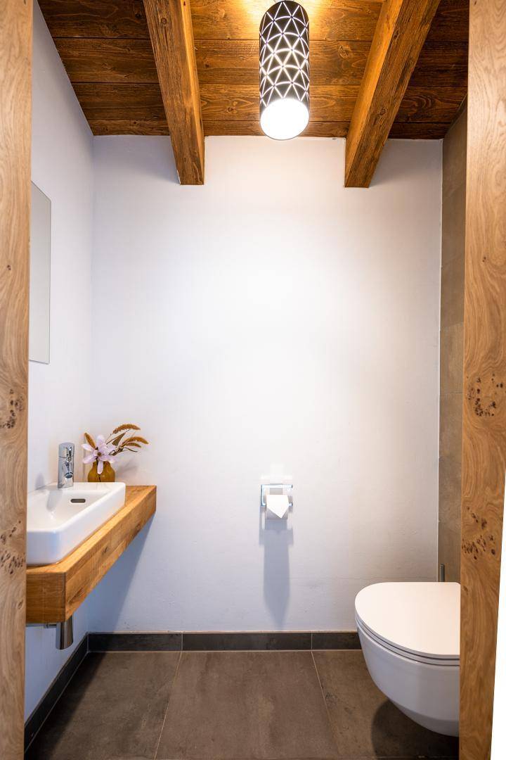 Kleines Gäste-WC mit modernem Waschbecken, Wand-WC und Holzbalkendecke.
