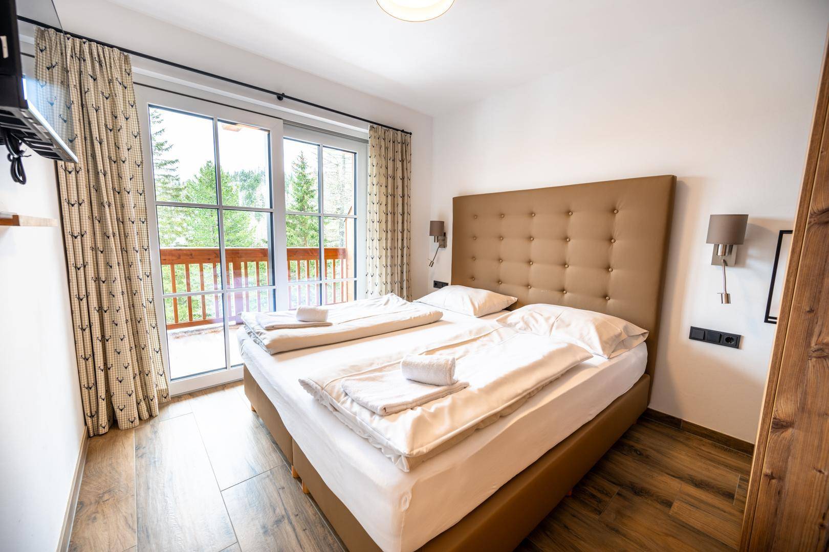 Schlafzimmer mit Doppelbett, großen Fenstern und direktem Zugang zum Balkon.