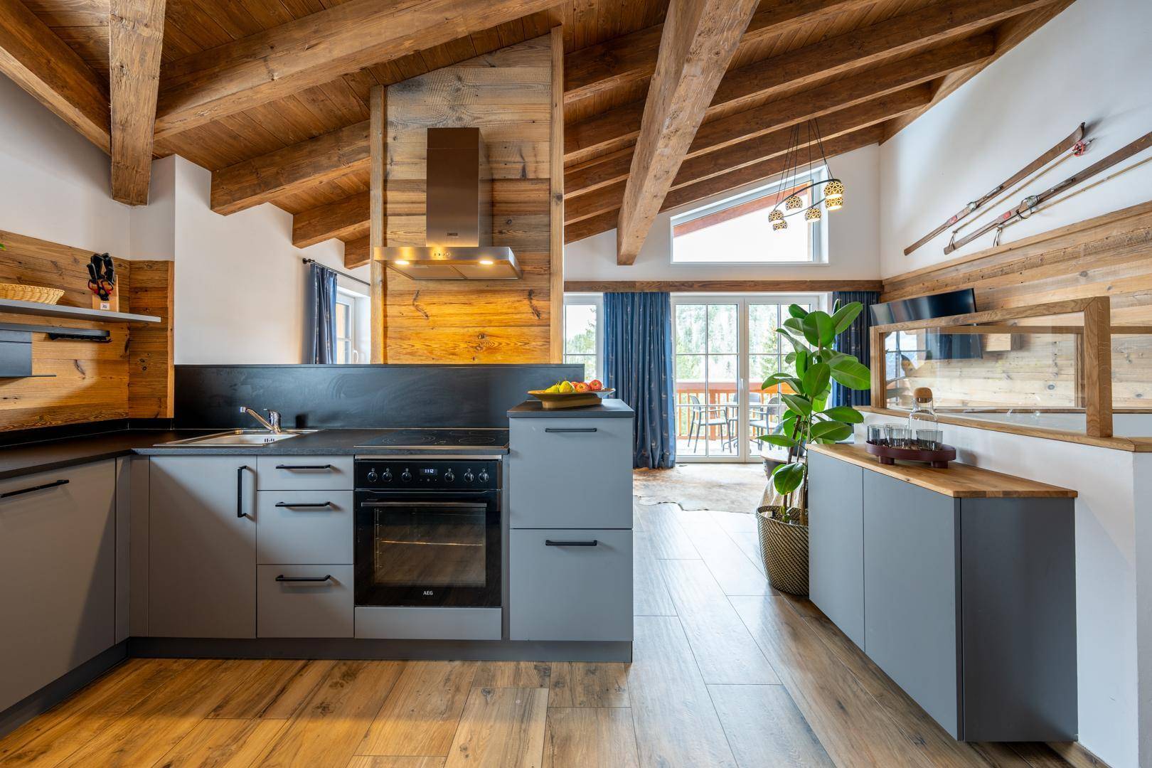 Moderne Küche mit grauen Schränken, Holzbalkendecke und Zugang zur Terrasse.