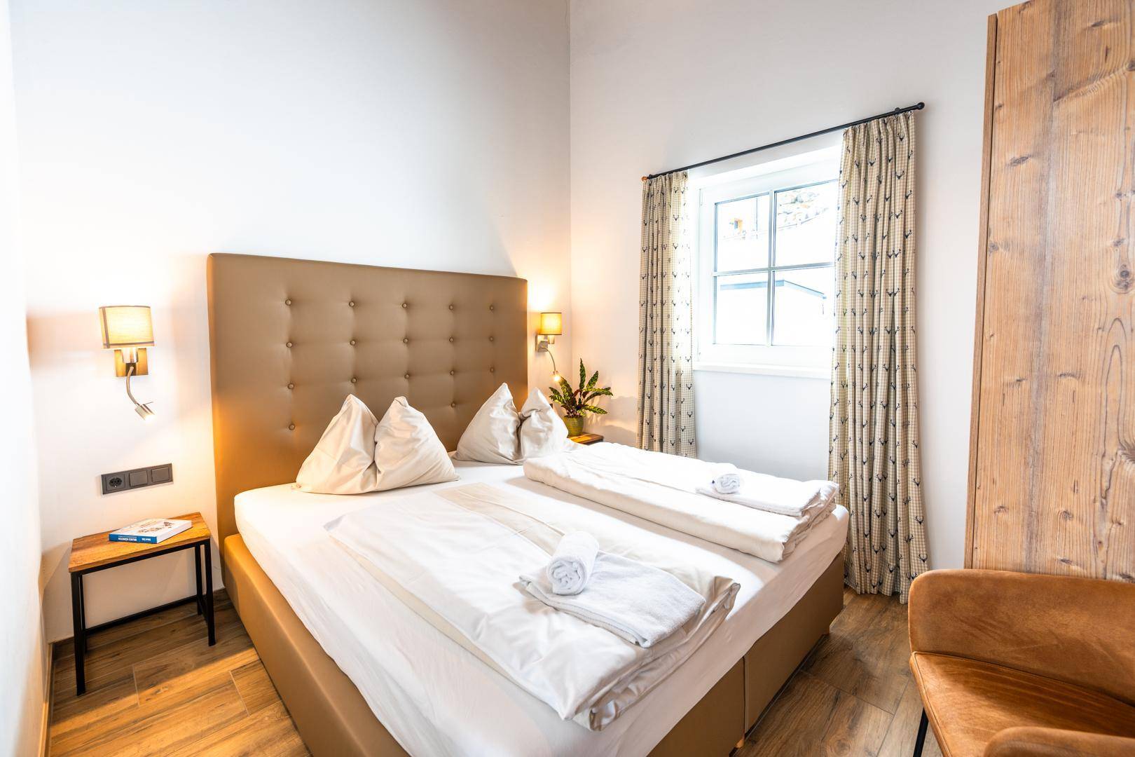 Helles Schlafzimmer mit Doppelbett, Holzboden und Fenster mit Blick nach draußen.