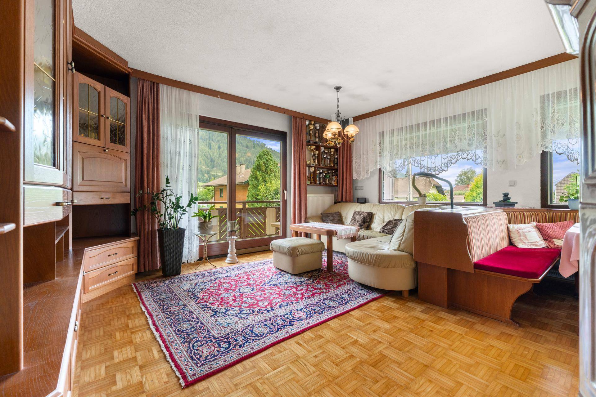 Traditionelles Wohnzimmer mit Parkettboden, großem Teppich und Zugang zum Balkon.