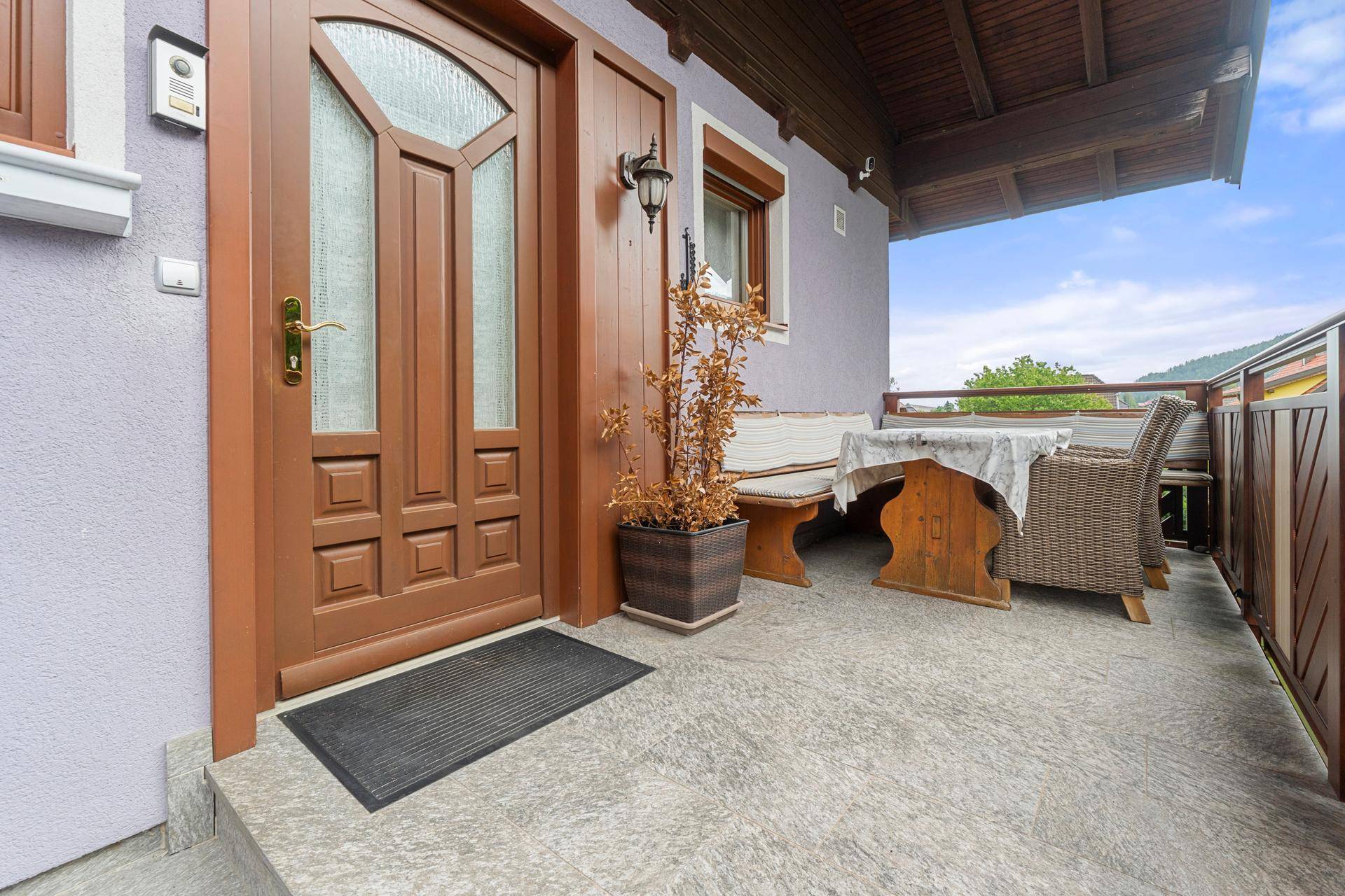 Eingangsbereich mit überdachter Terrasse, Holztür und Sitzgelegenheiten.