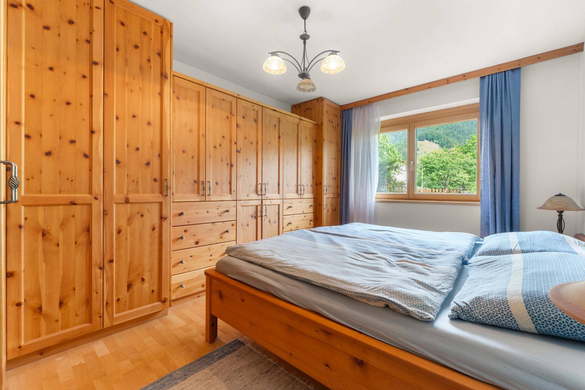 Schlafzimmer mit Holzbett, Einbauschränken und Blick ins Grüne.