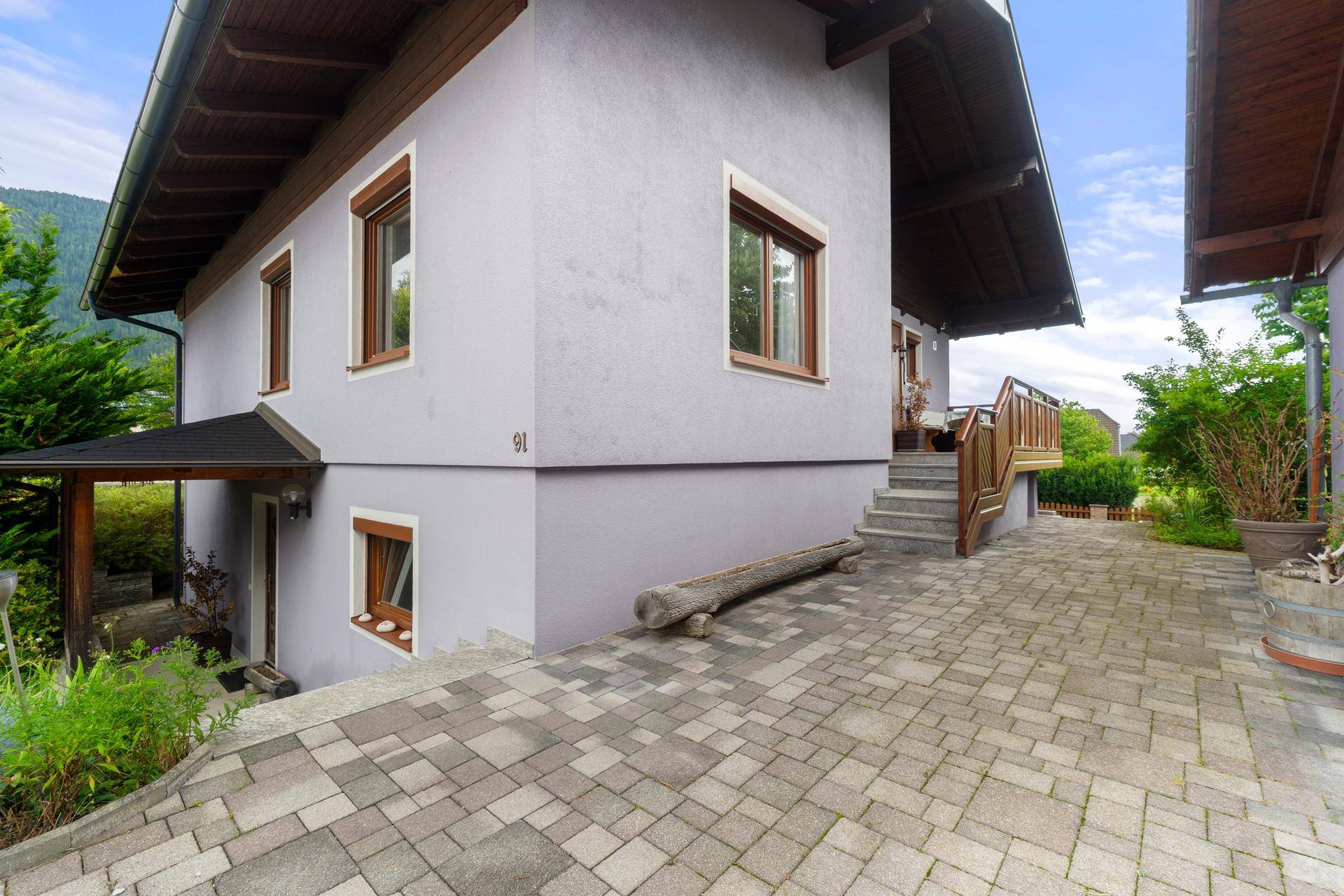 Seitenansicht des Hauses mit gepflastertem Weg und Zugang zum Untergeschoss.