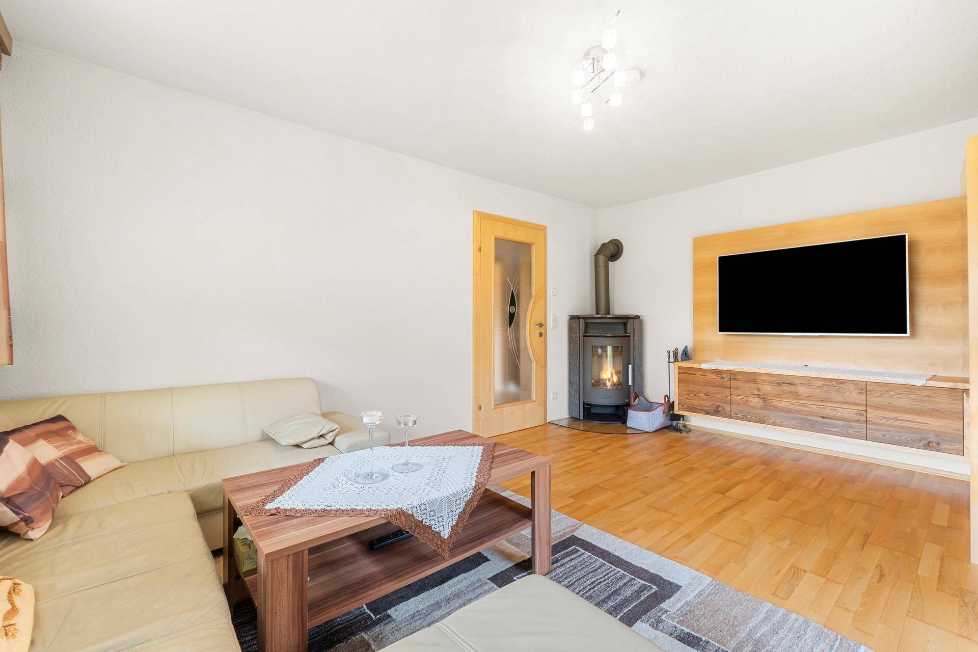 Gemütliches Wohnzimmer mit Holzboden, Kaminofen und moderner TV-Wand.