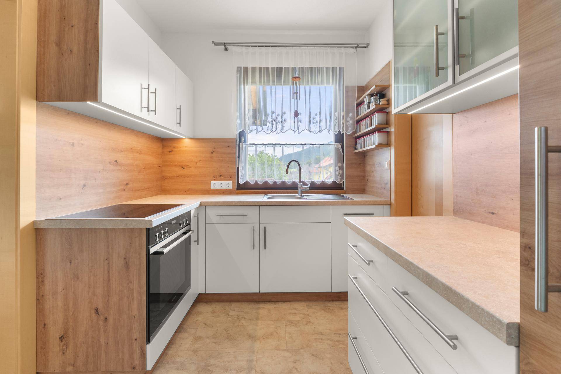 Helle Küche mit modernen Holz- und weißen Schränken, integriertem Backofen und Fenster.